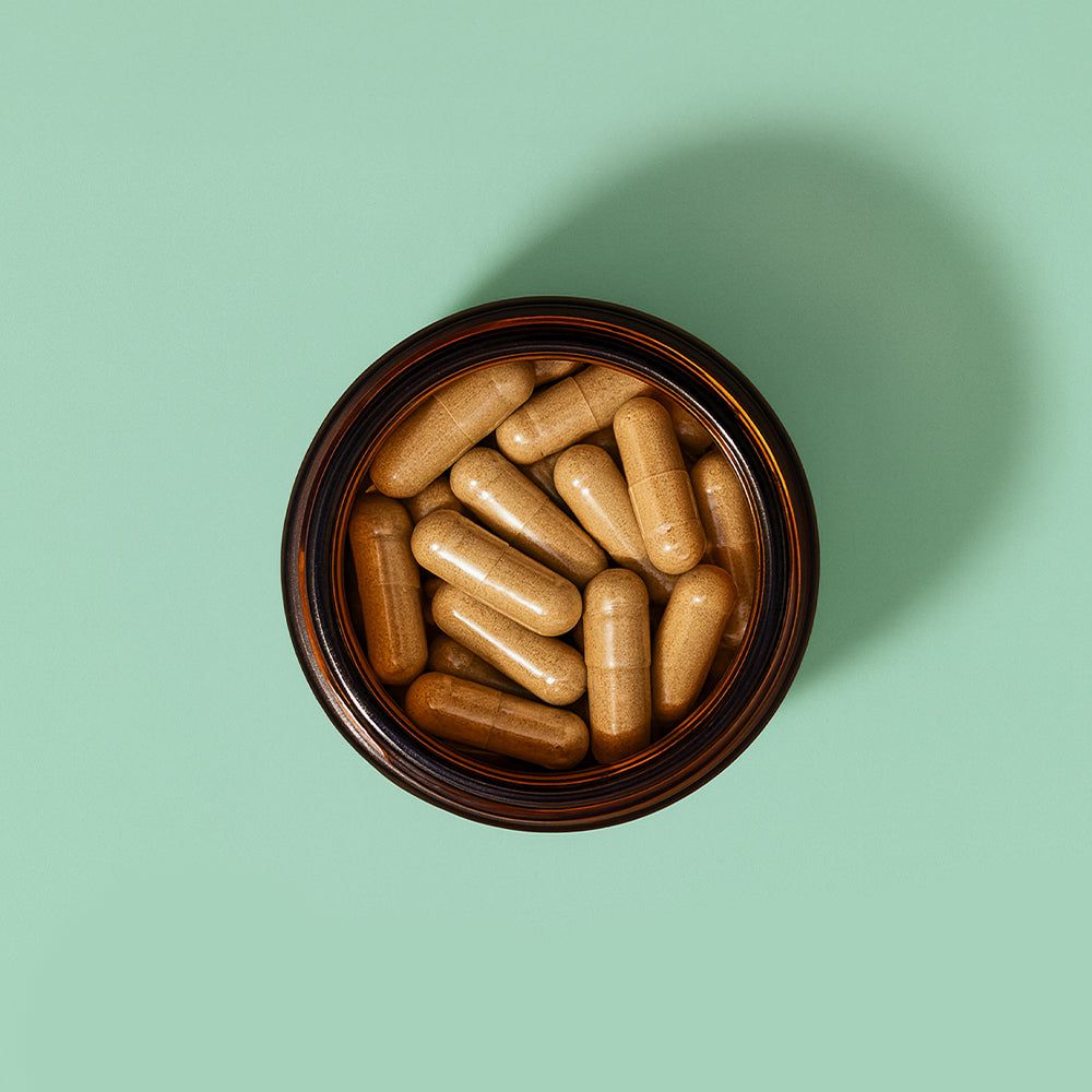 Draufsicht auf eine braune Glasdose mit braunen Kapseln. Grüner Hintergrund.