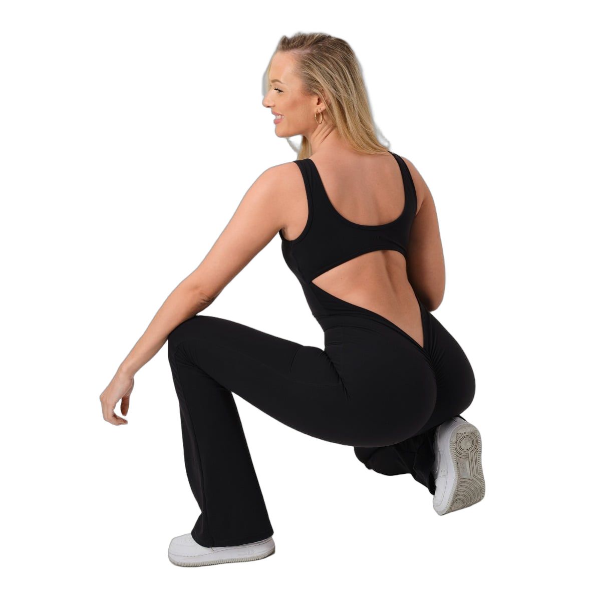 Frau in schwarzem ärmellosem Jumpsuit hockt, seitliche Ansicht.