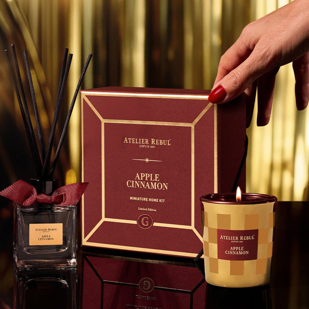 Geschenkset mit Kerze, Duftdiffusor und Box. Rote Box mit goldener Umrandung. Kerze brennt. Atelier Rebul-Logo.