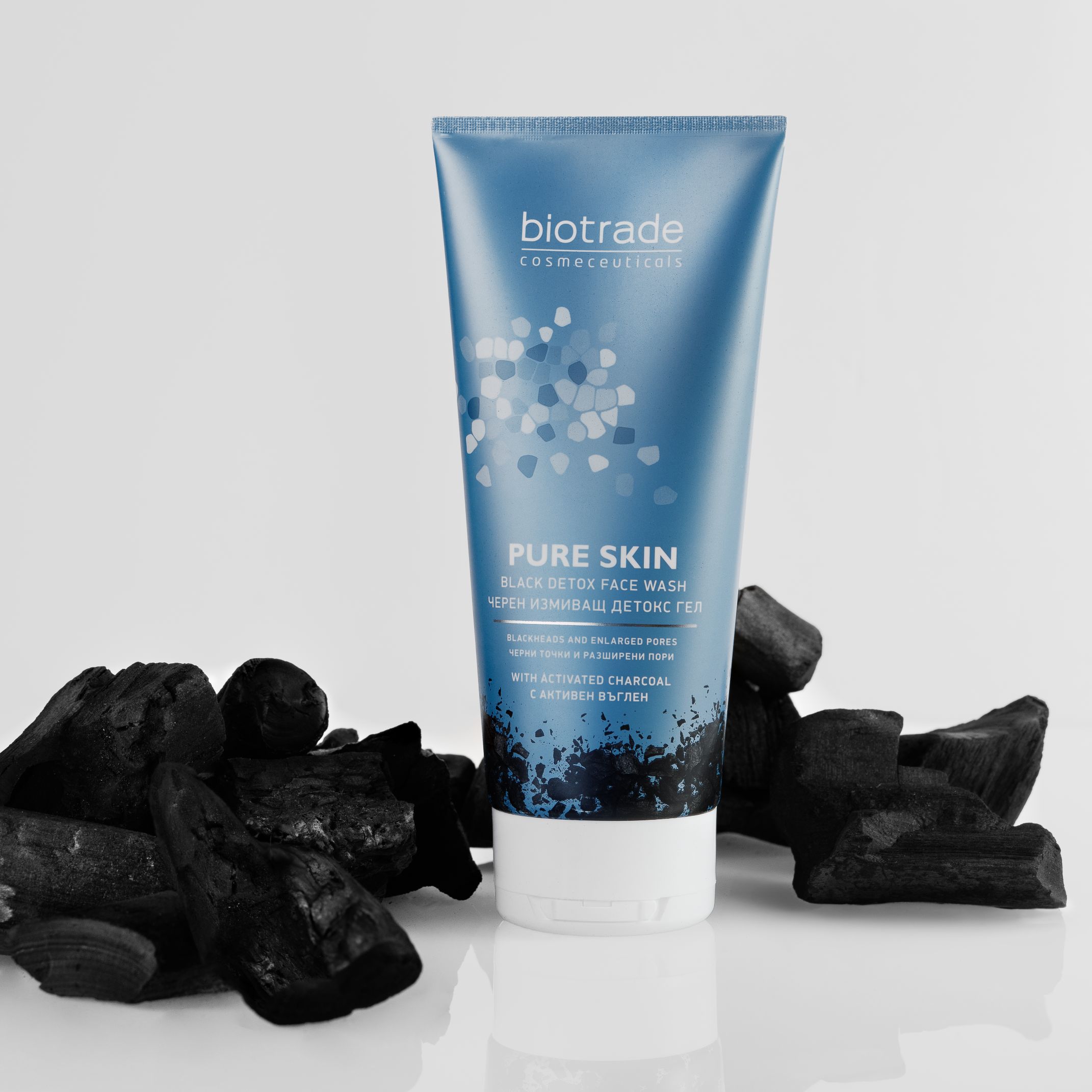 Blaue Tube mit Produktnamen und Text. Umgeben von Holzkohle. Aufschrift: Pure Skin Black Detox Gesichtswaschgel.
