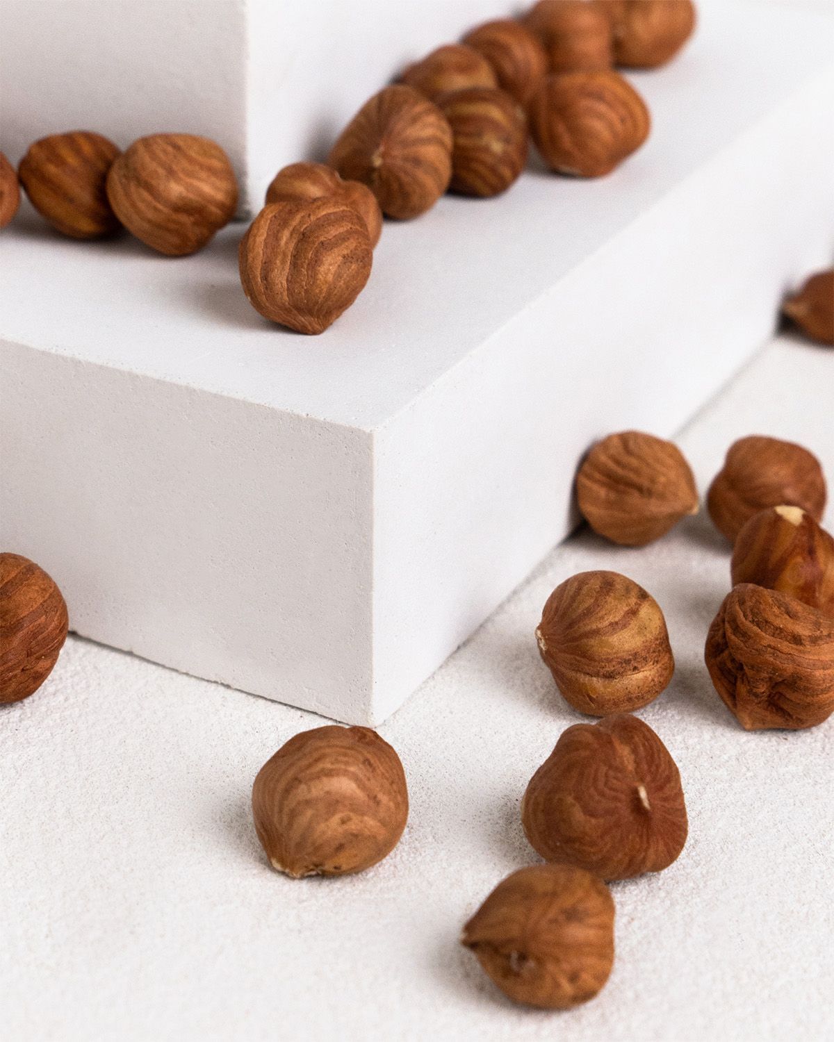 Haselnüsse auf weißem Podest. Gebräunte Farbe, ovale Form, leicht geriffelte Oberfläche.