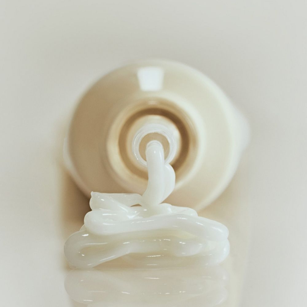 Nahaufnahme: Creme tritt aus einer hellbeigen Tube. Auf hellem Hintergrund. Creme-Tube liegt.