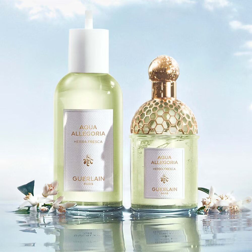 Zwei Guerlain Aqua Allegoria Herba Fresca Flakons. Ein Flakon mit Sprühkopf, einer mit goldfarbenem Verschluss, im Wasser.