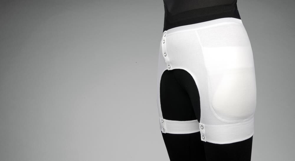 Weißer Hüftprotektor-Slip mit Knöpfen und Polsterung. Seitliche Beinriemen. Auf schwarzer Kleidung getragen.