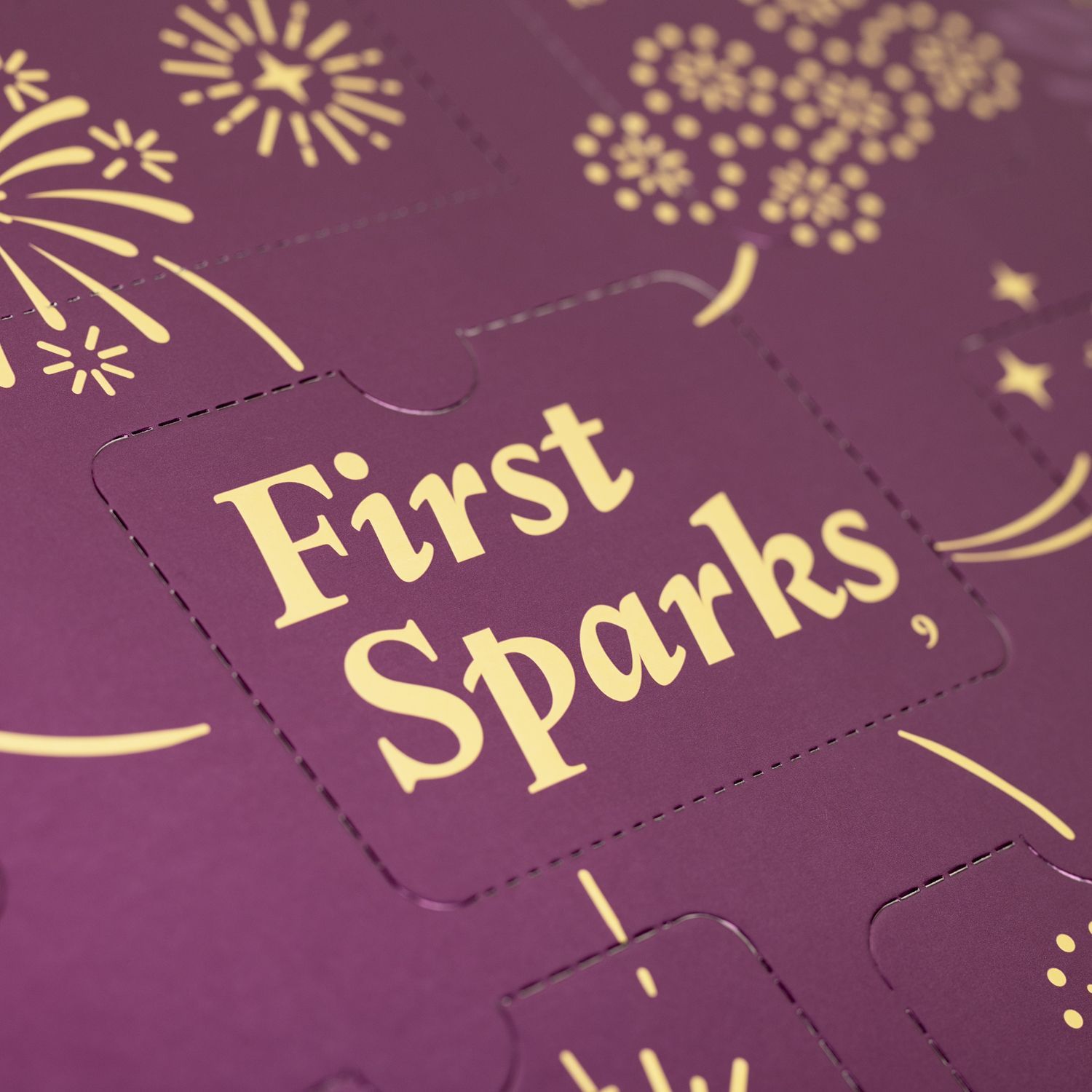 Nahaufnahme des Adventskalenders. Goldener Text: First Sparks. Illustrationen von Feuerwerk.