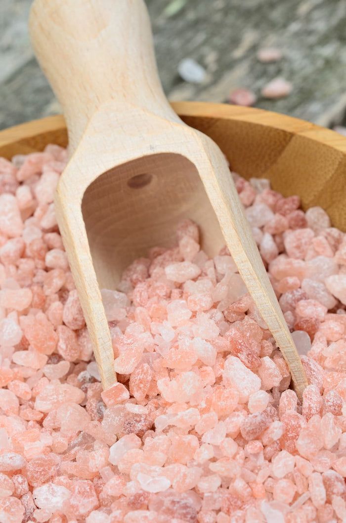 Holzschaufel in einer Schüssel mit rosa Kristallen. Die Schaufel ist aus hellem Holz gefertigt.
