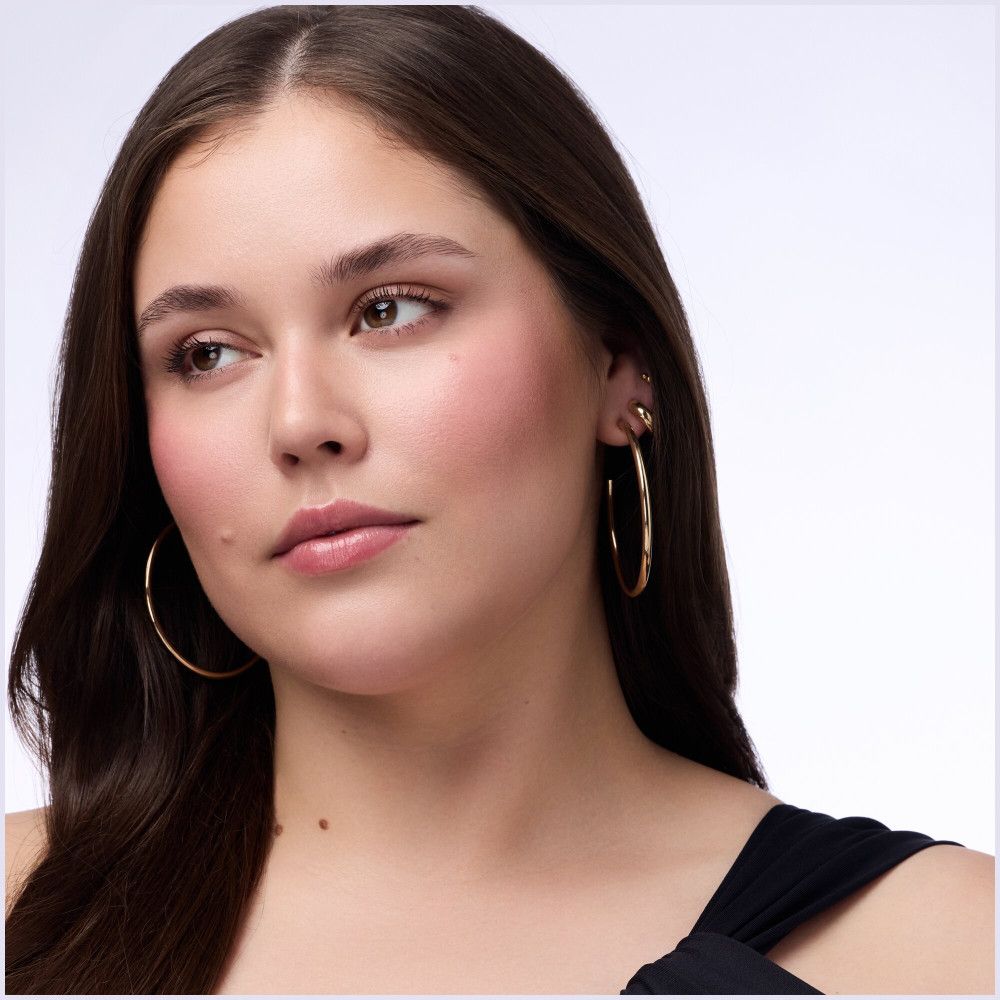 Porträt einer Frau mit gebräunter Haut und rosigem Rouge auf den Wangen. Sie trägt goldene Creolen.