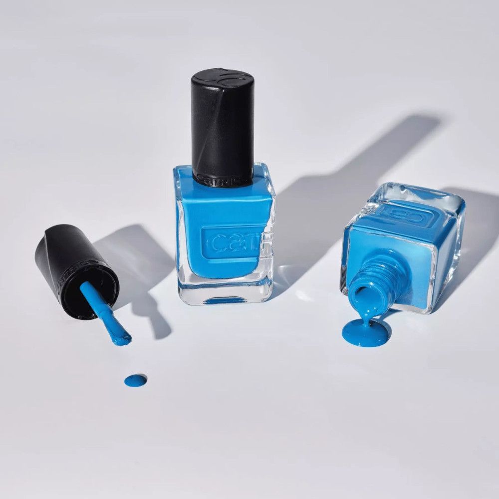 Drei Nagellackflaschen, eine mit Deckel, eine umgekippt, eine aufrecht. Blauer Nagellack ist verschüttet. Der Markenname ist sichtbar.