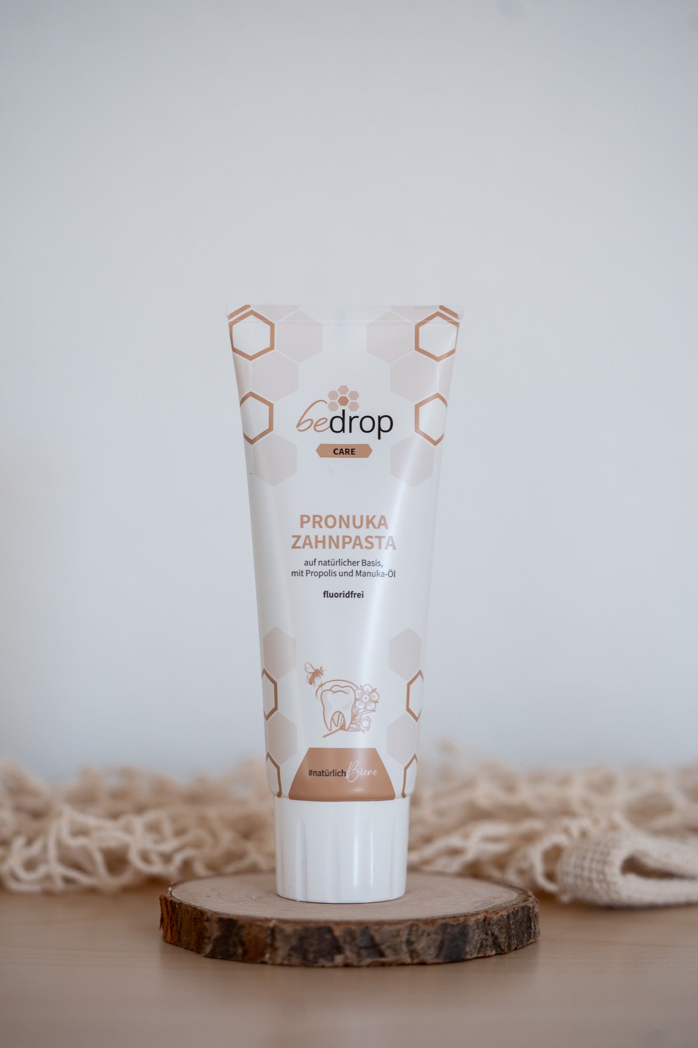 Tube bedrop Pronuka Zahnpasta auf Holzscheibe. Weiße Tube mit braunen Schriftzügen und Bienen-Motiv. Fluoridfrei.