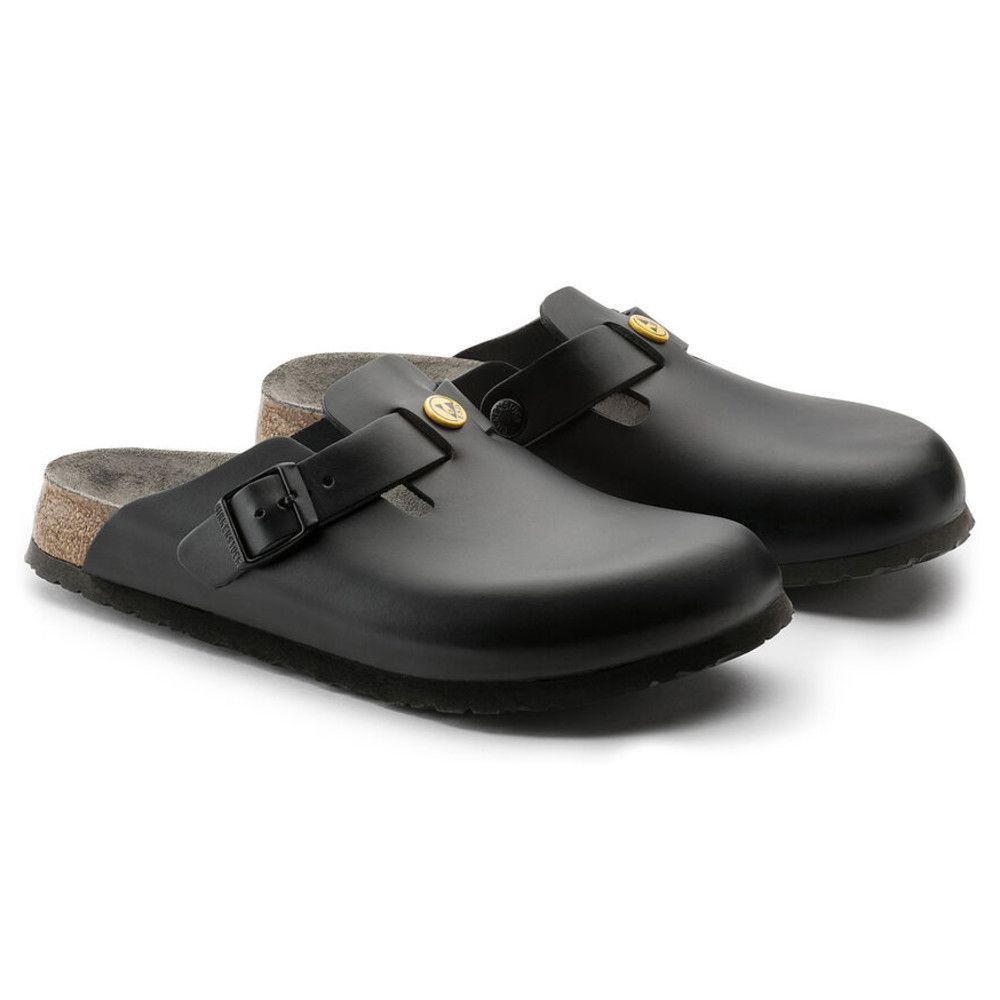 Zwei schwarze Birkenstock Boston ESD-Schuhe. Riemen mit Schnalle. Gelbes ESD-Symbol. Korkfußbett. Schuhe stehen nebeneinander.