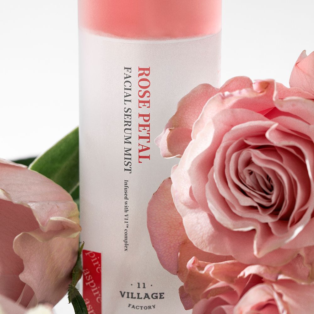 Produktflasche mit Rosen. Text: ROSE PETAL FACIAL SERUM MIST. Marke: VILLAGE 11 FACTORY. Rosenblüten umgeben die Flasche.