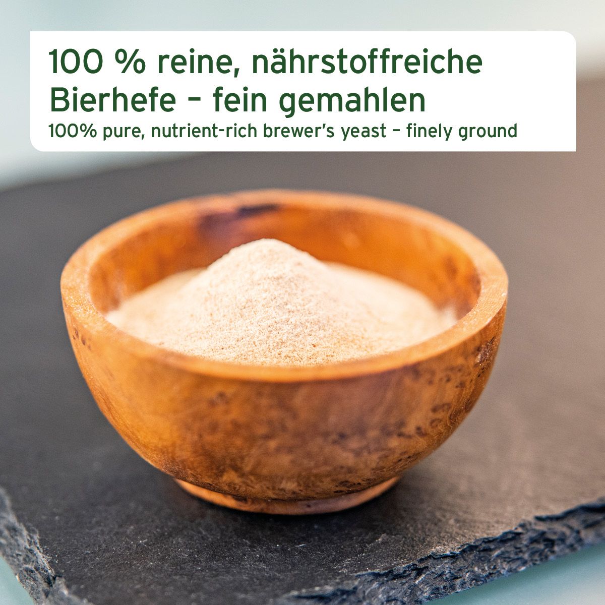 Hölzerne Schale mit fein gemahlenem, hellbraunem Bierhefepulver auf dunklem Untergrund.