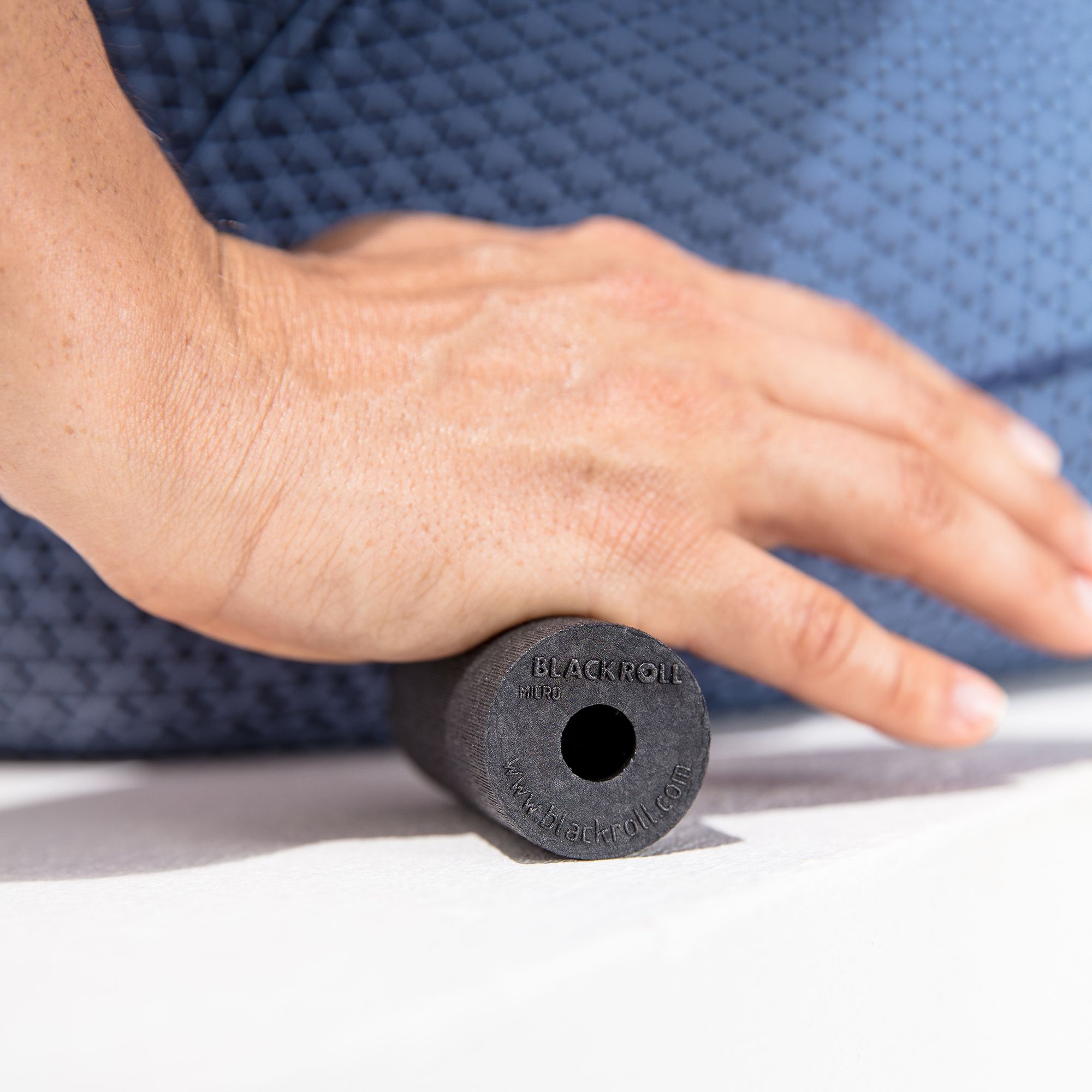 Hand auf schwarzer, zylindrischer Faszienrolle. Aufschrift: BLACKROLL. Zentrales Loch.