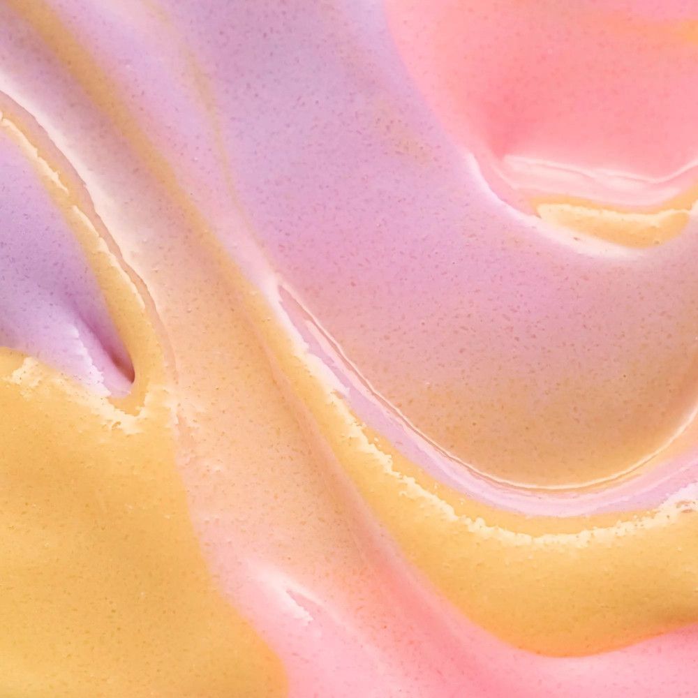 Nahaufnahme von Zuckerpeeling in Gelb, Rosa und Lila. Die Textur ist cremig und gewirbelt.