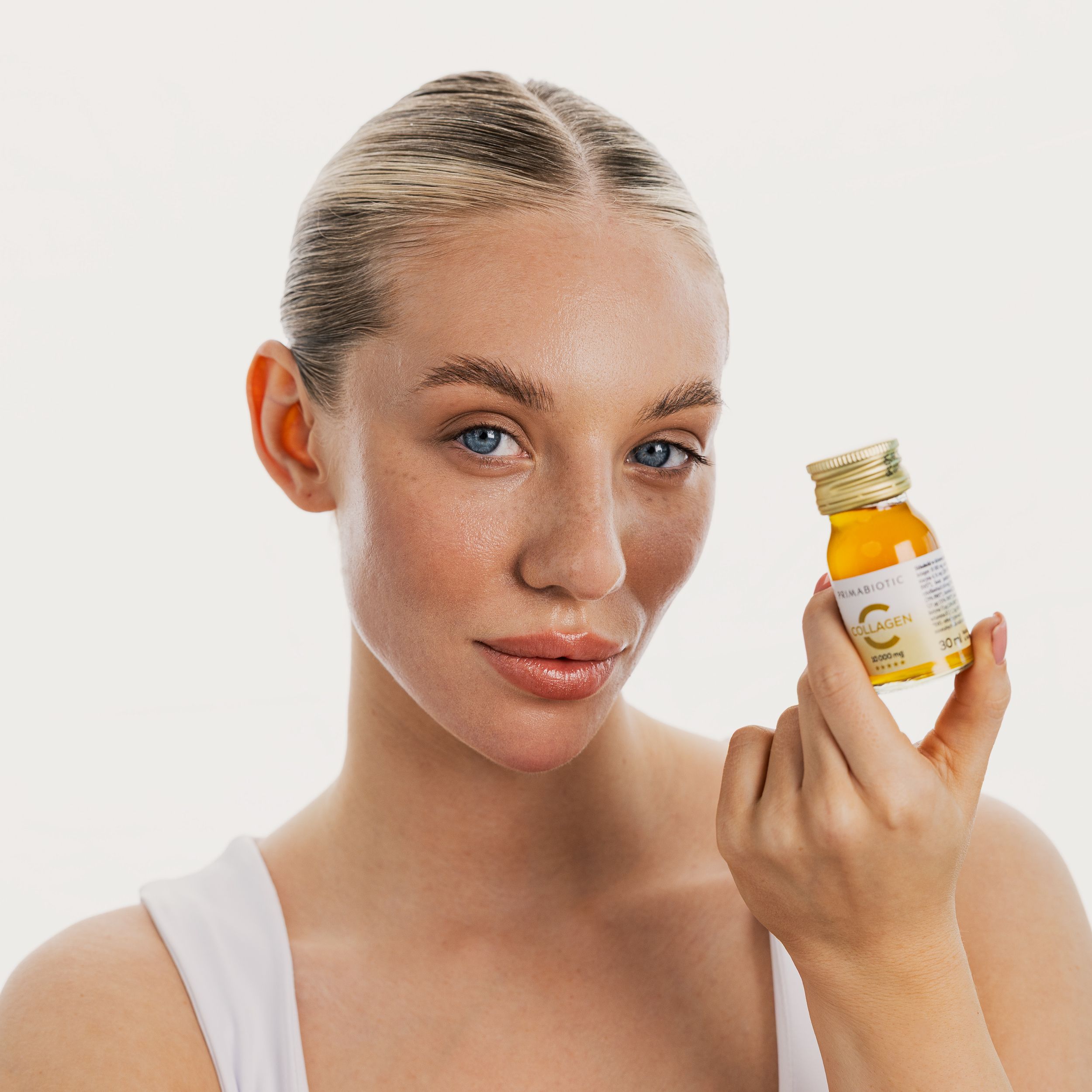 Frau hält eine Flasche Primabiotic Collagen. Goldfarbener Deckel, Etikett mit Schriftzug. Frau mit blonden Haaren und blauen Augen.