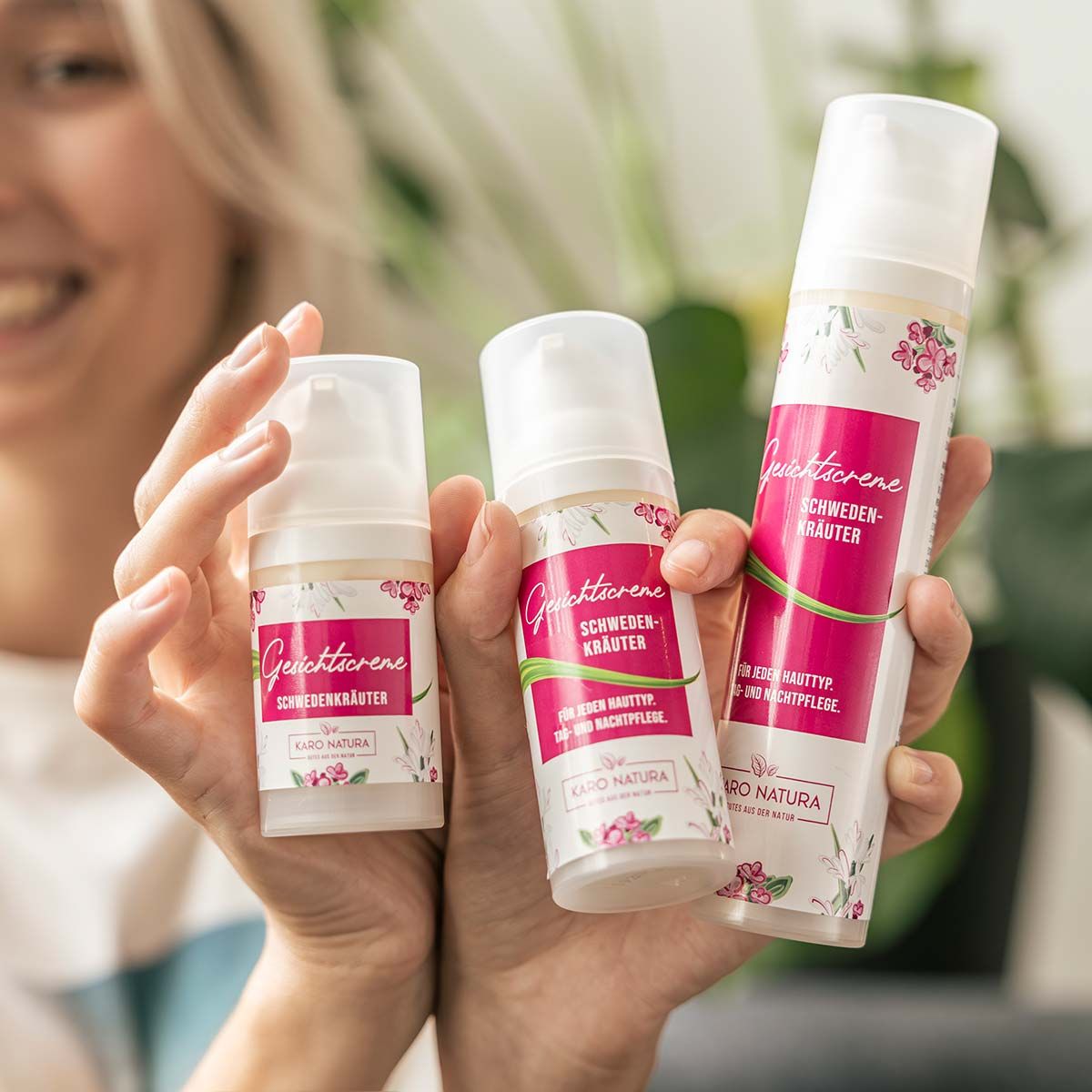 Drei weiße Flaschen mit pinkfarbener Banderole. Text: Gesichtcreme, Schwedenkräuter, Karo Natura. Tag- und Nachtpflege. Frau hält Flaschen.