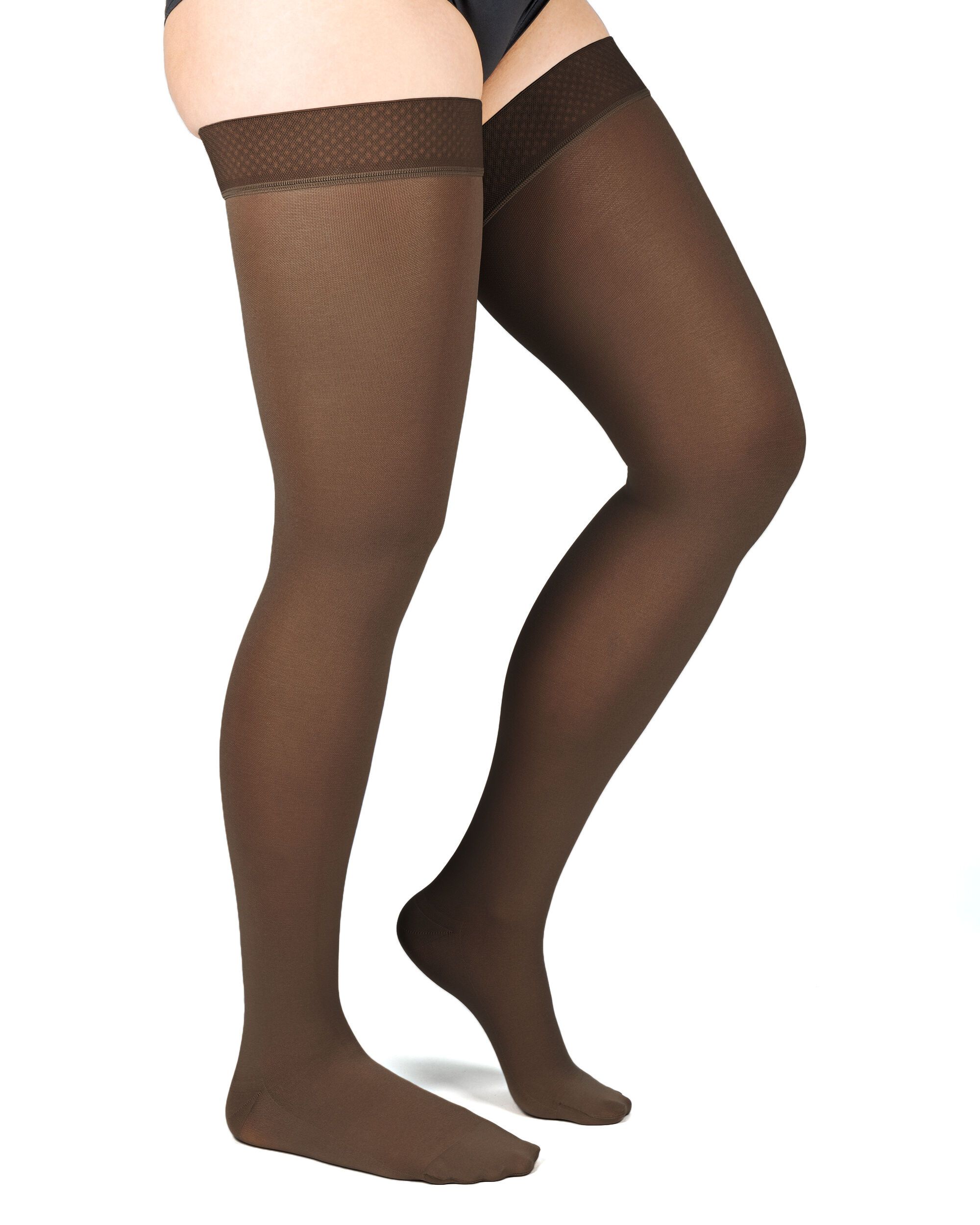 Braune Kompressions-Schenkelstrümpfe. Oberschenkelband mit Muster. Blick von der Seite auf Beine und Füße.