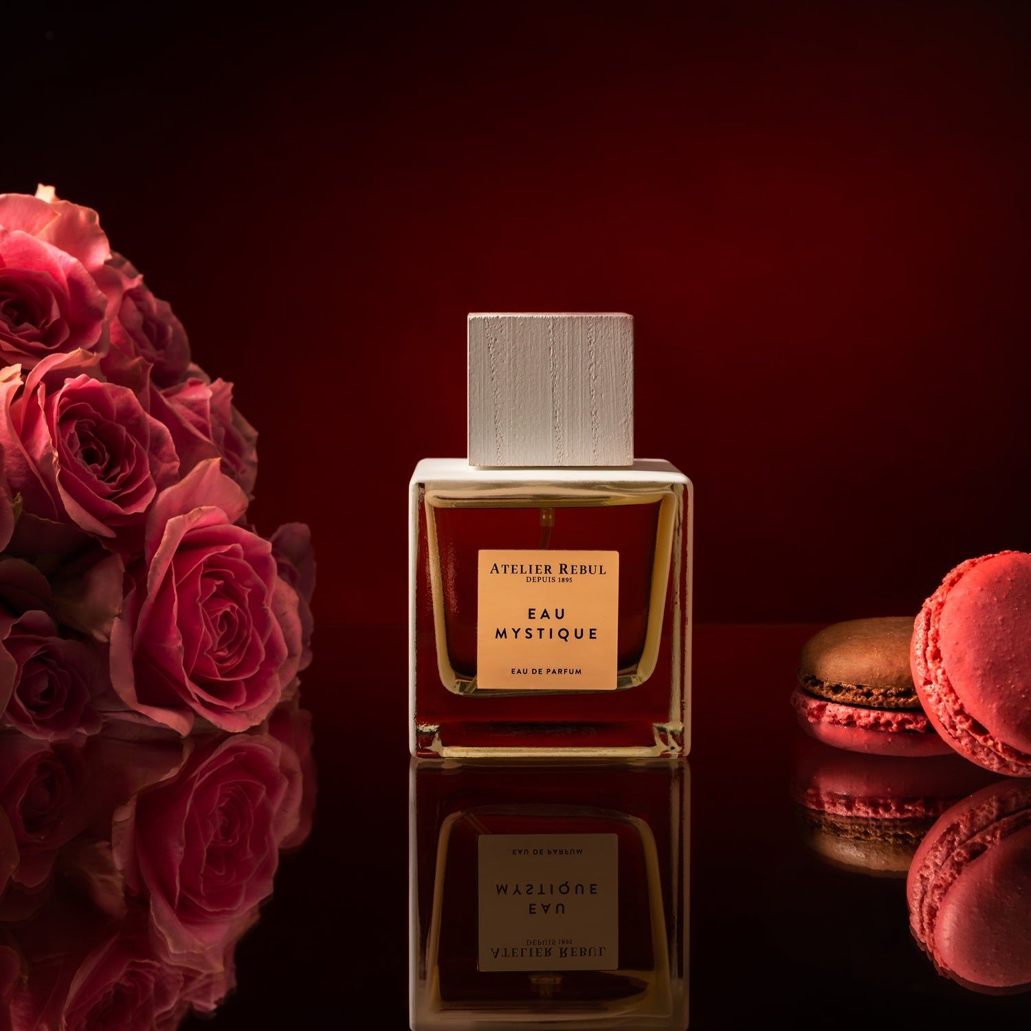 Parfümflakon mit quadratischem Etikett. Rosen und Makronen im Hintergrund. Aufschrift: Eau Mystique Eau de Parfum.