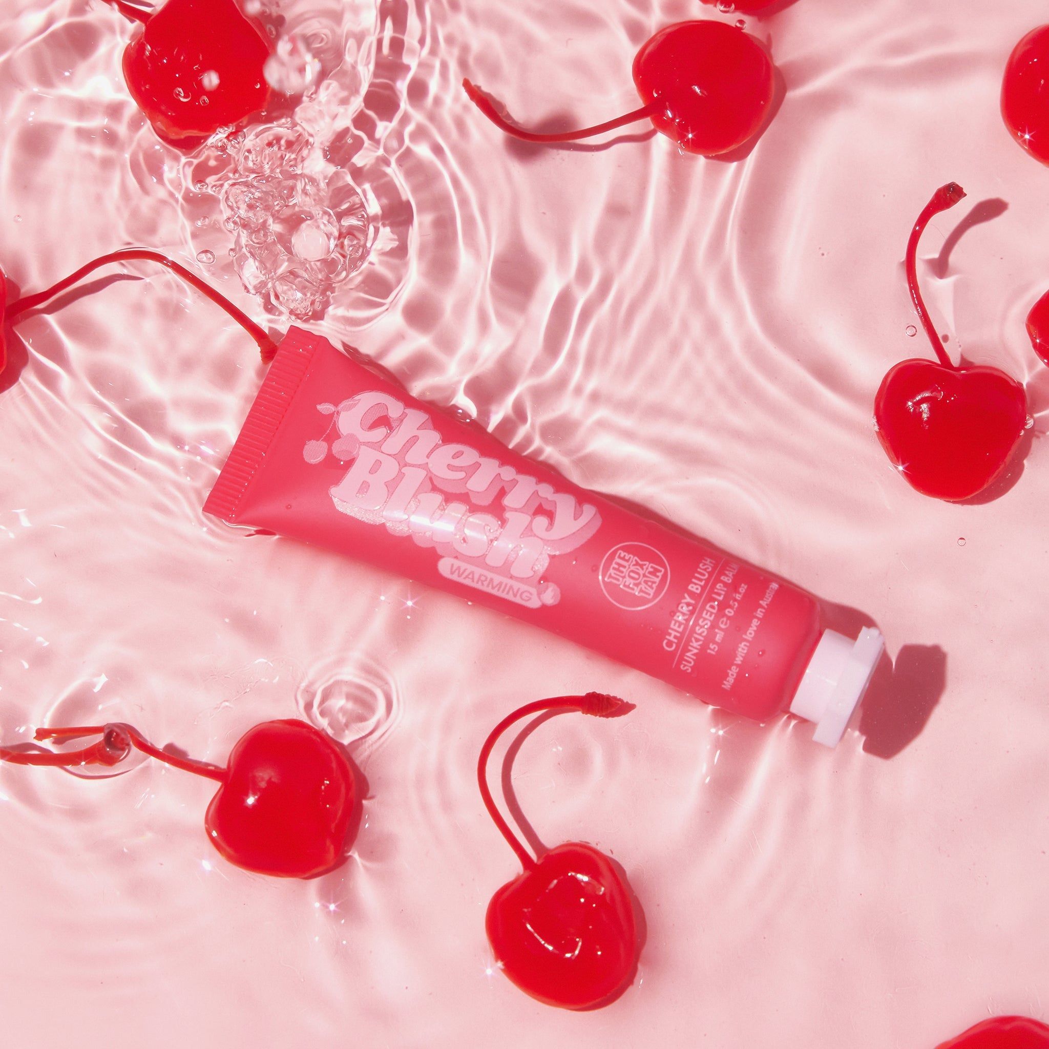 Rote Tube 'Cherry Blush' in Wasser mit Kirschen. Produktname und Marke sichtbar. Weißer Verschluss.