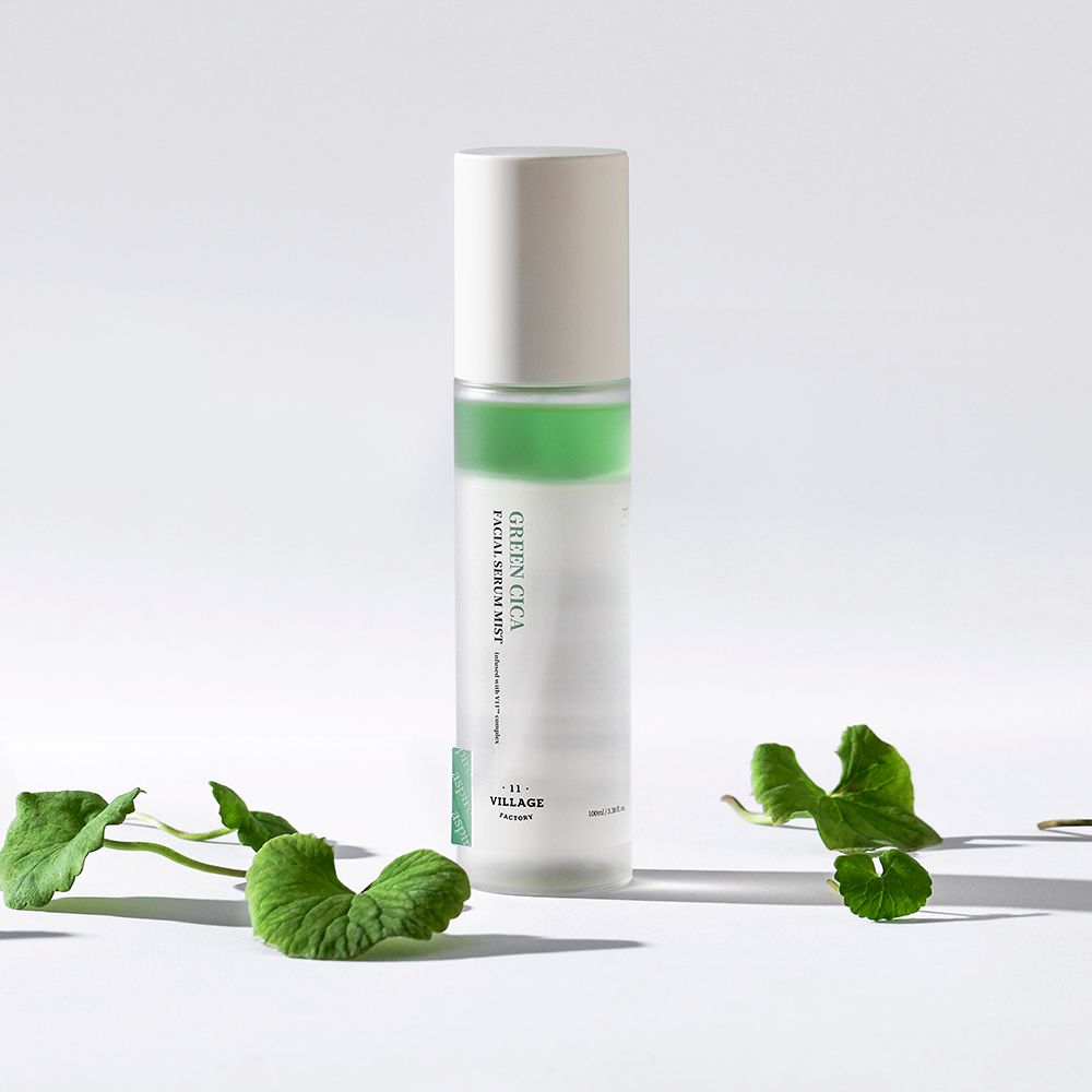 Zylindrische Flasche mit grünem Streifen und weißem Deckel. Beschriftung: Green Cica Facial Serum Mist. Marke: Village 11 Factory. Mit Blättern.