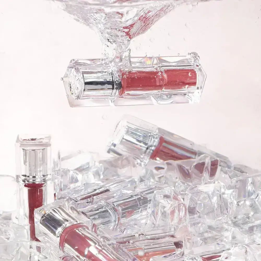 Mehrere Lippen-Tints in transparenten Behältern mit silbernen Deckeln, die in Eiswürfeln liegen.
