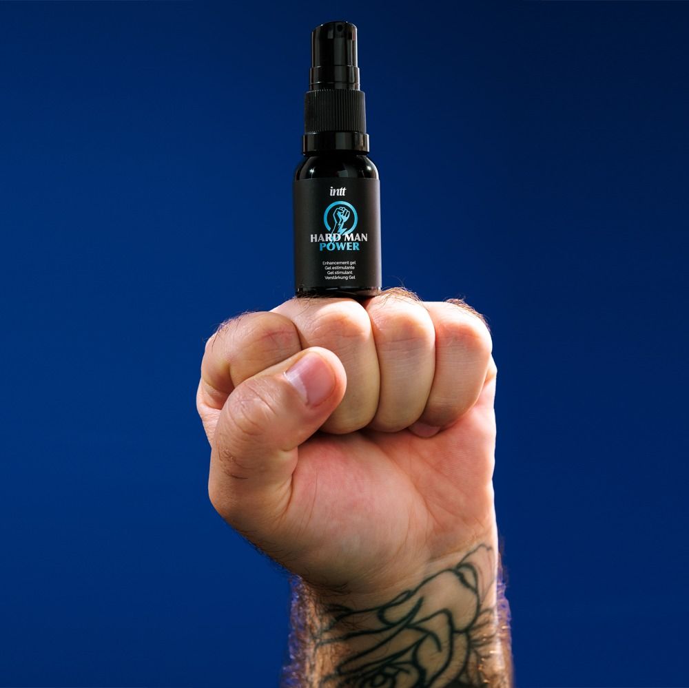 Faust hält eine Sprühflasche 'Hard Man Power' vor blauem Hintergrund.
