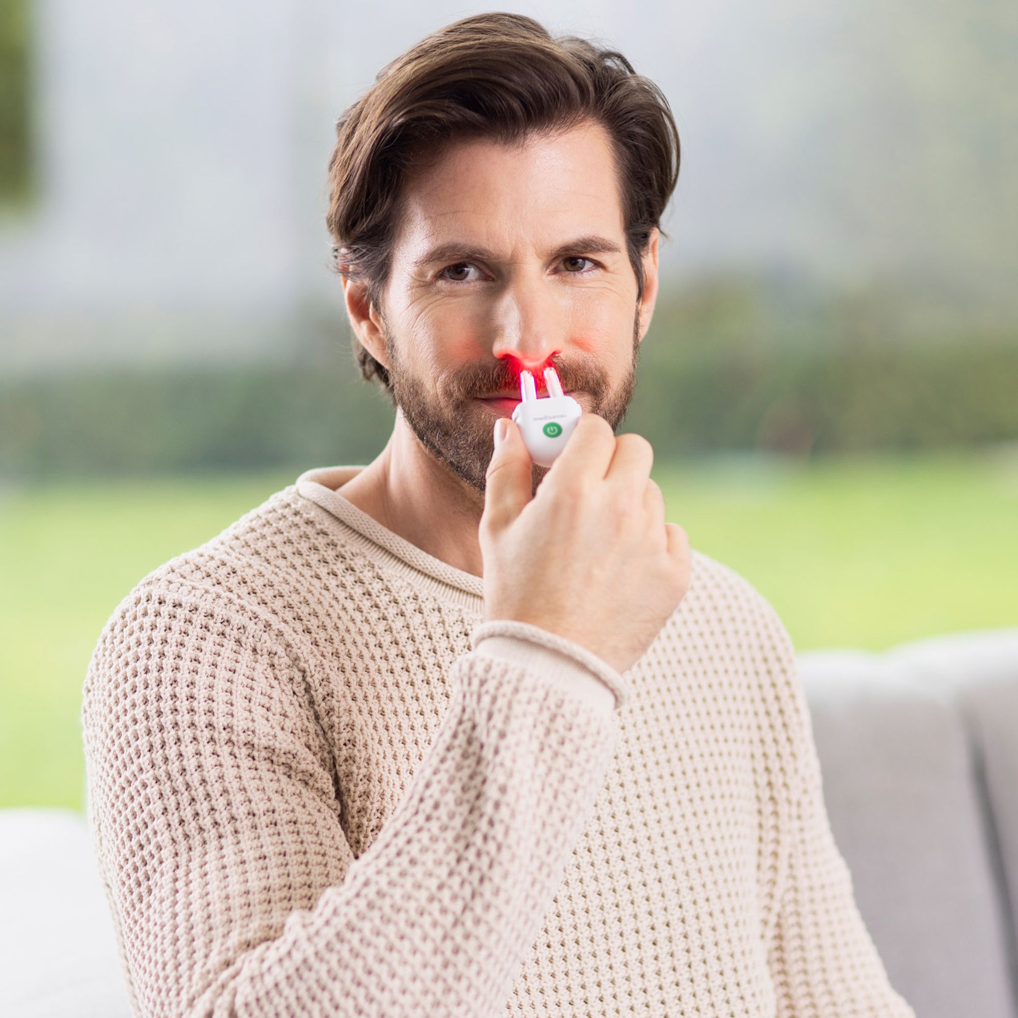 Mann hält weißes Gerät an die Nase. Rote Lichter an den Nasenlöchern. Beige Pullover.