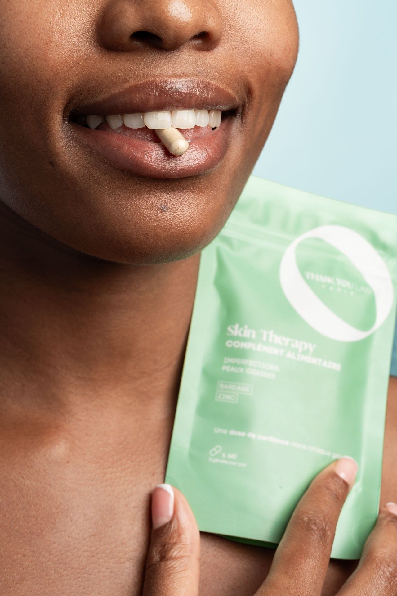 Person hält eine Kapsel im Mund und eine grüne Verpackung. Text: Skin Therapy, Complément Alimentaire.
