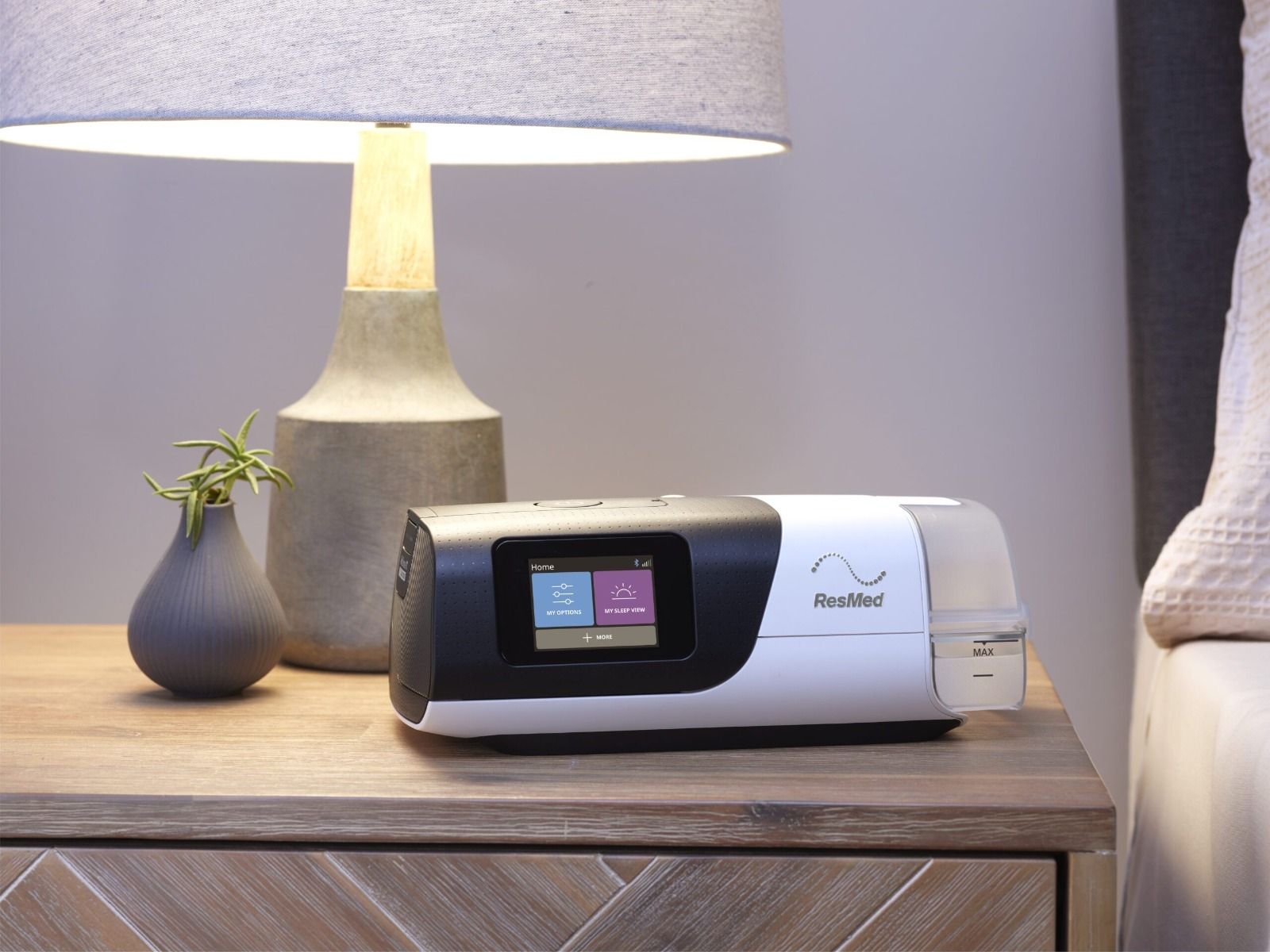 ResMed AirSense 11 auf Nachttisch neben Lampe und Vase.