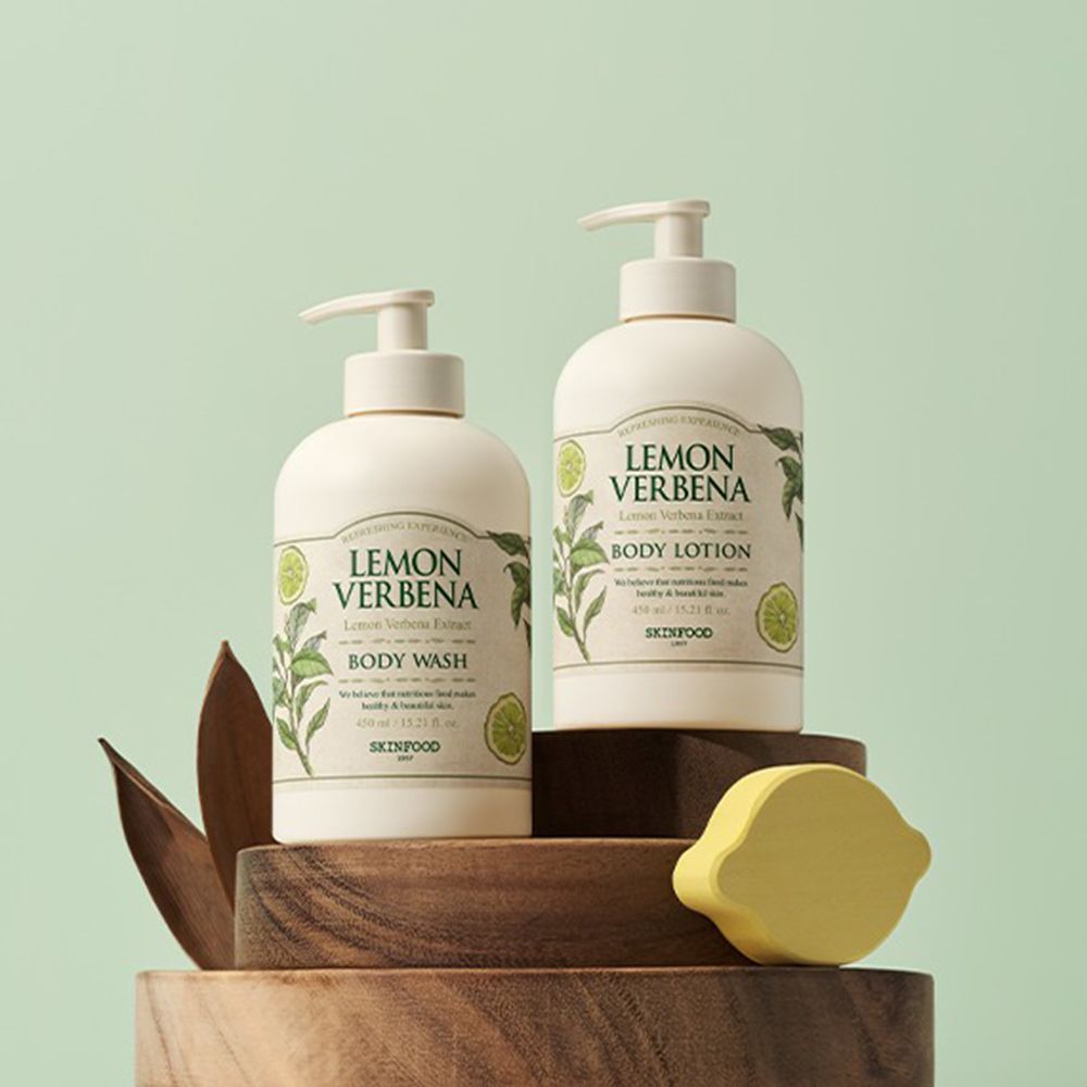 Zwei SKINFOOD Lemon Verbena Produkte auf Holzpodest. Body Wash und Body Lotion Flaschen. Zitronen-Dekoration.