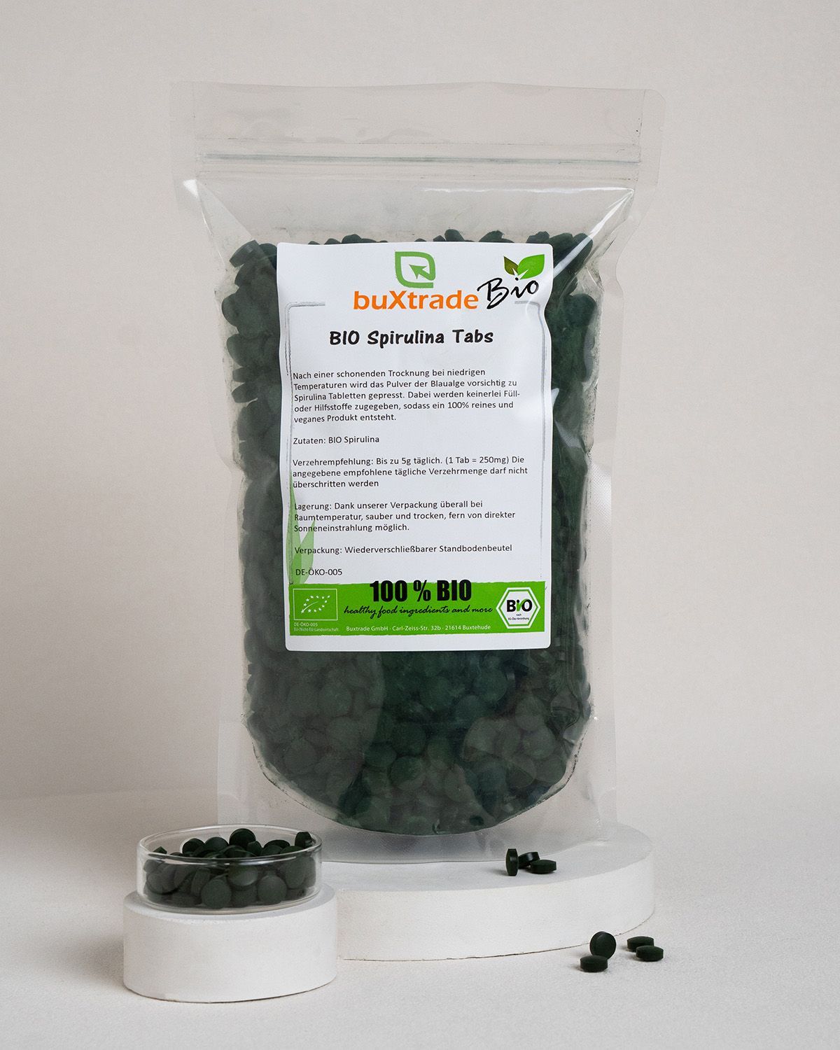 Transparente Tüte mit Tabletten, daneben kleine Dose und Tabletten. Aufdruck 'buXtrade Bio Spirulina Tabs' und Bio-Siegel.