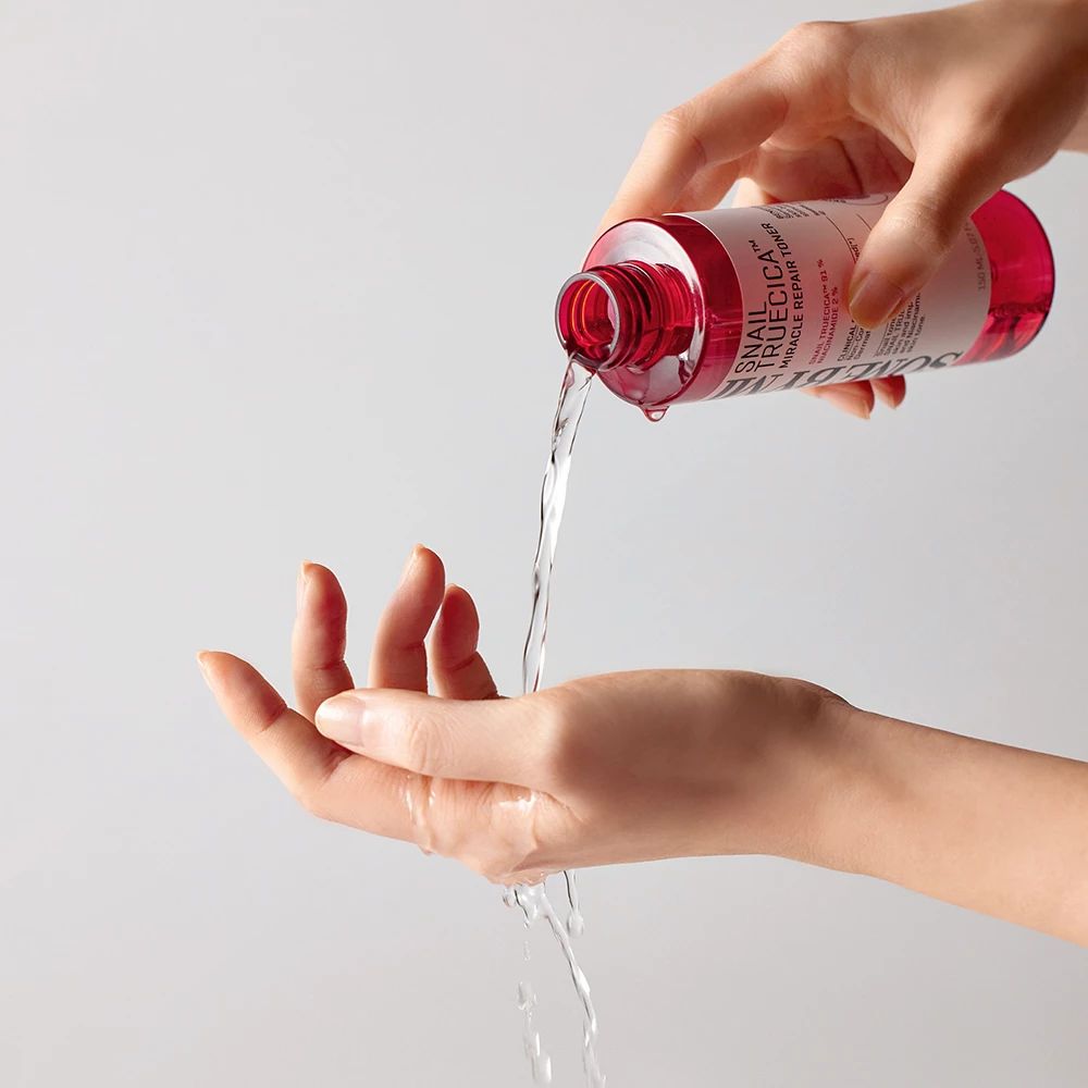 Eine Hand hält eine Flasche, aus der Flüssigkeit in die andere Hand gegossen wird. Die Flasche ist rot und trägt die Aufschrift SOME BY MI.