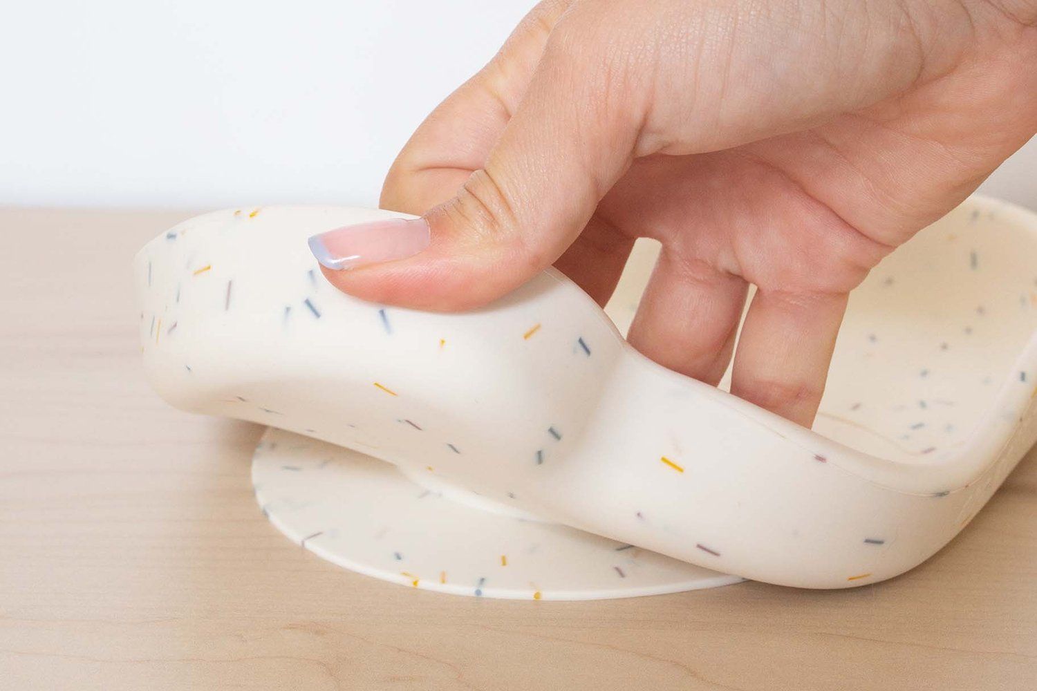 Hand hebt Teller an. Beige Teller mit bunten Punkten. Runde Form.