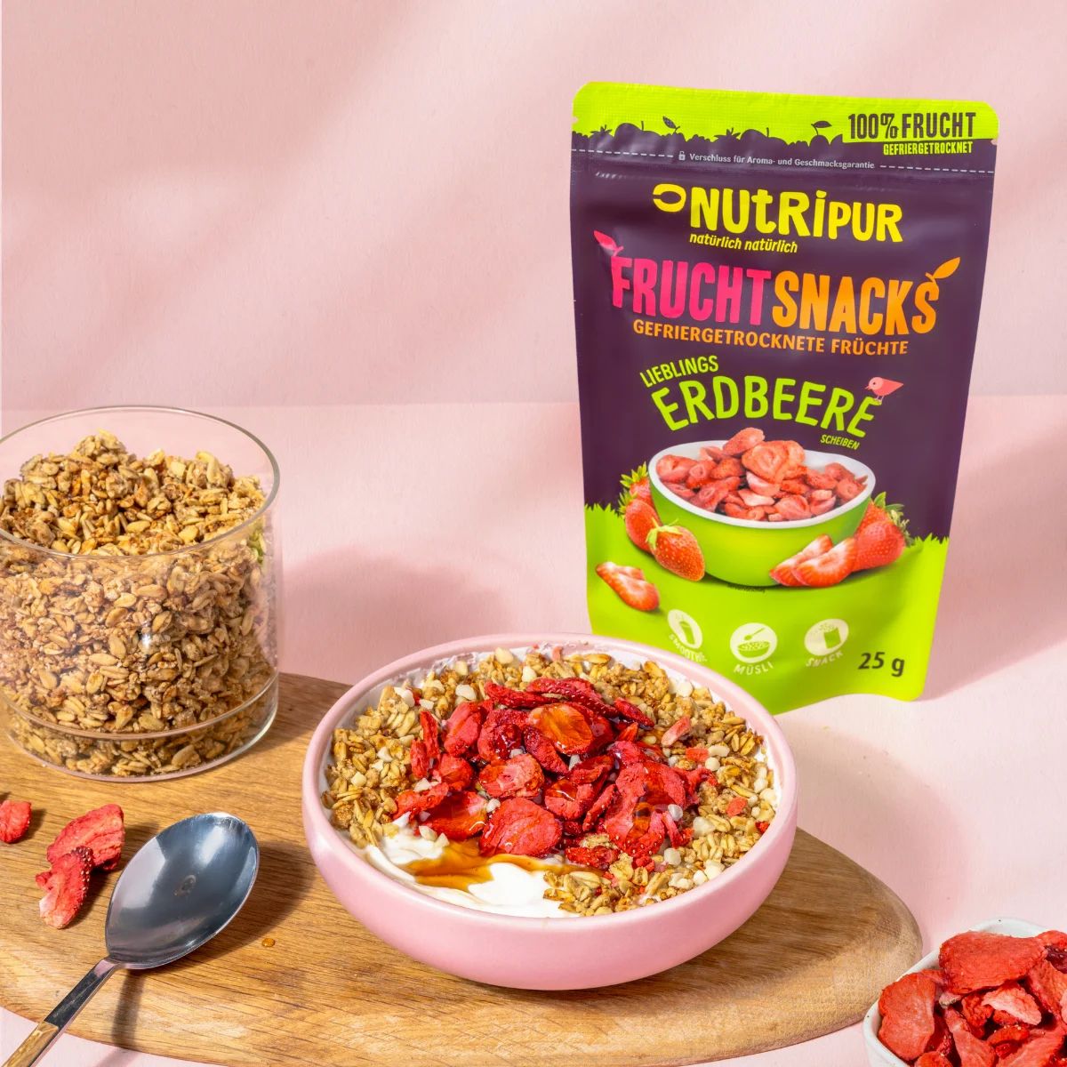 Gefriergetrocknete Erdbeeren in einer Schüssel und auf einem Müsli. Daneben ein Beutel mit der Aufschrift NutriPur Fruchtsnacks Erdbeere.