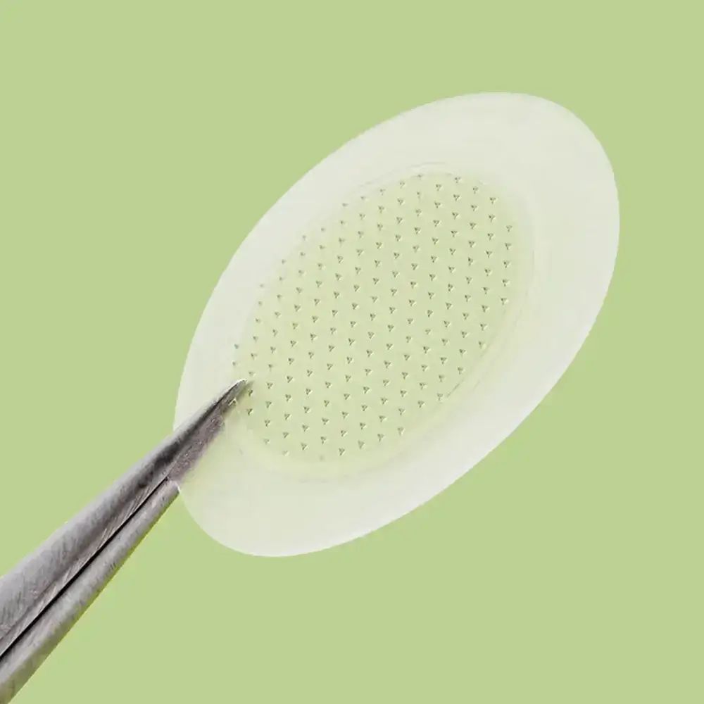 Nahaufnahme eines Pflasters mit Mikro-Spitzen. Pinzette greift das Pflaster. Hintergrund grün.