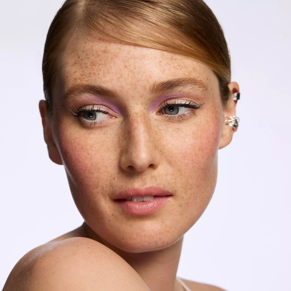 Porträt einer Frau mit lila Lidschatten. Haut mit Sommersprossen, helle Augen.