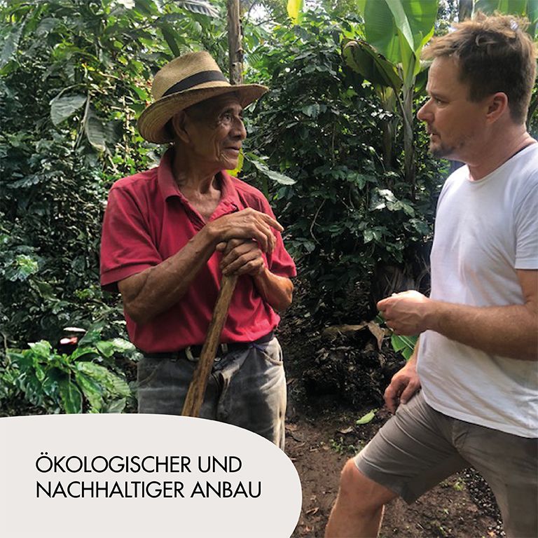 Zwei Männer in einem Kaffeeanbaugebiet. Mann mit Hut und Mann mit weißem T-Shirt.