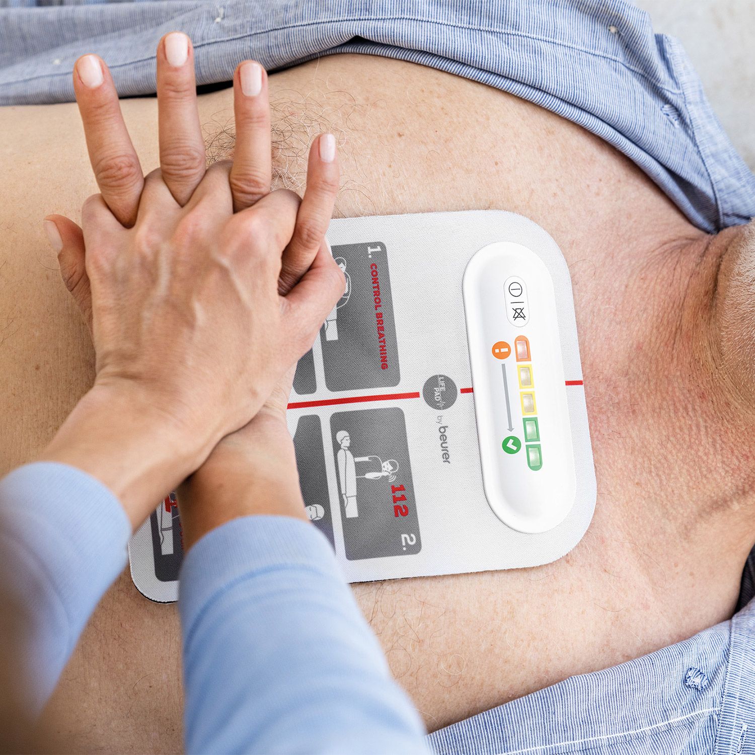 Reanimationshilfe auf Brustkorb. Gerät mit Bedienfeld und Piktogrammen. Marke: beurer. Person führt Herzdruckmassage durch.