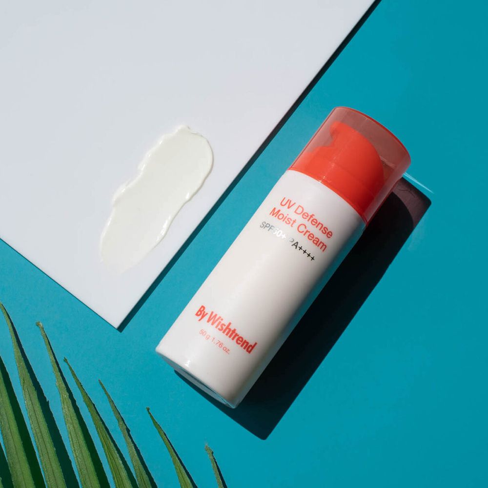 Sonnencreme-Flakon neben Creme-Klecks auf weißem Papier, auf blauem Hintergrund. Marke: By Wishtrend. Aufschrift: UV Defense Moist Cream SPF50+ PA++++.