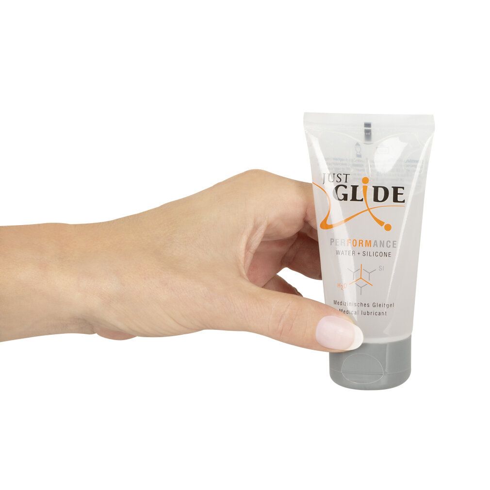Hand hält eine transparente Tube mit grauer Kappe. Aufschrift: JUST GLIDE PERFORMANCE WATER + SILICONE. Text: Medizinischer Gleitgel.