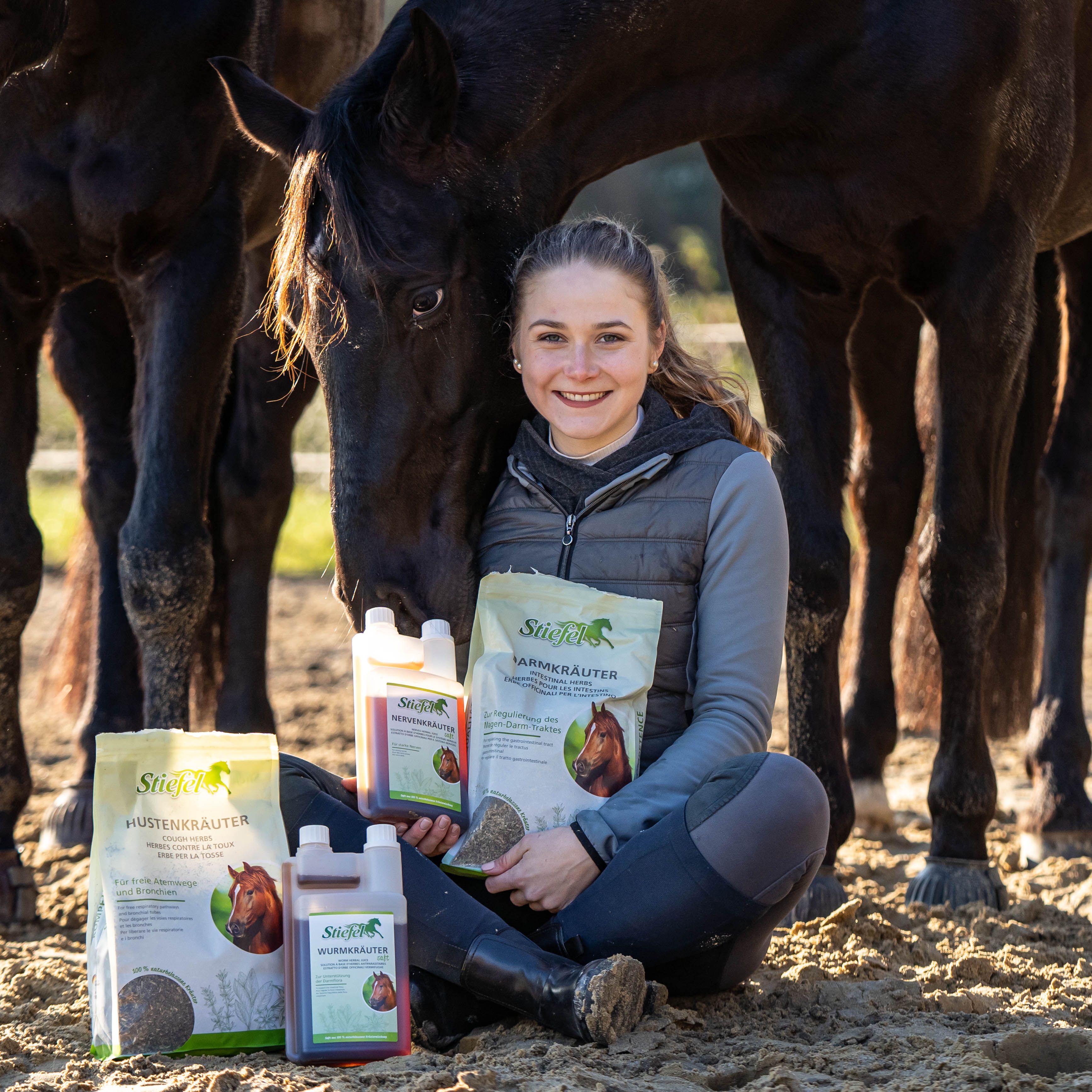 Frau mit Stiefel Hustenkräuter-Beutel und Flaschen. Produkte mit Pferdekopf-Logo. Frau sitzt neben Pferden.