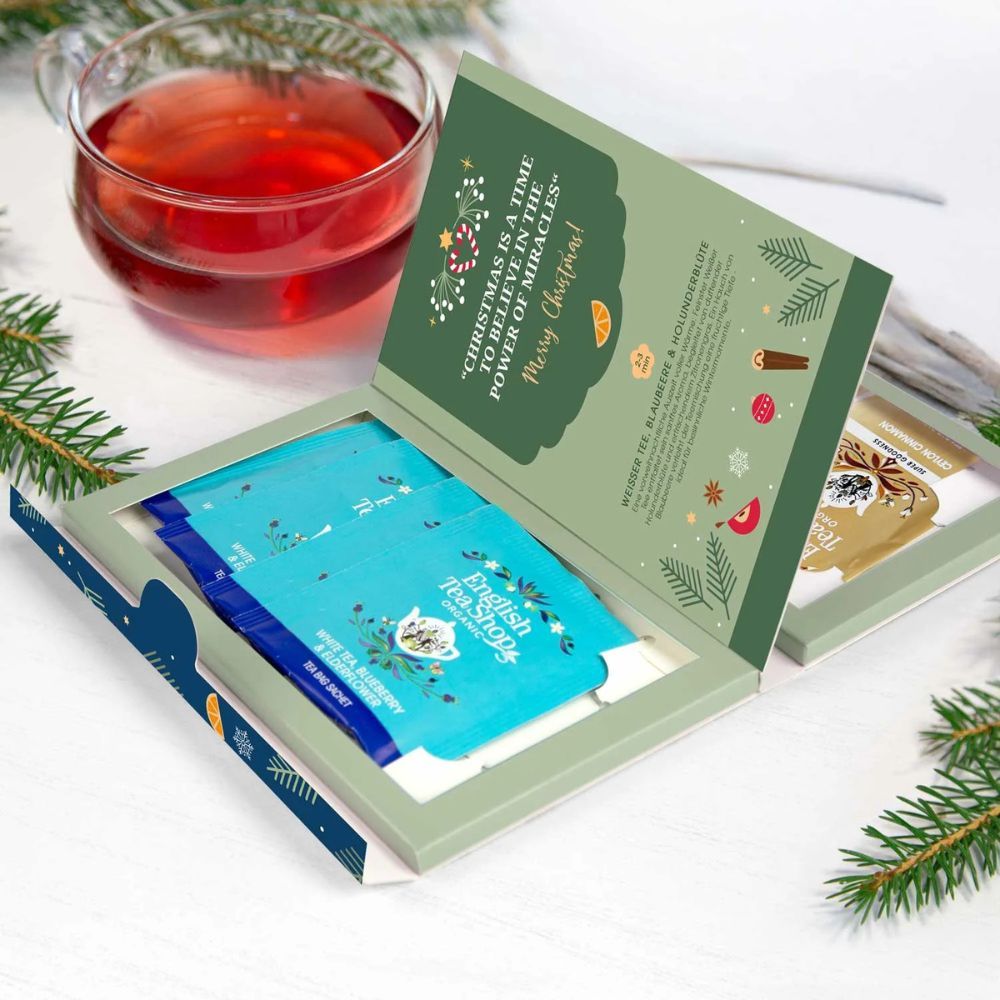 Geöffnete Geschenkbox mit Teebeuteln und einer Tasse Tee. Grüne Innenseite mit weihnachtlichem Design. English Tea Shop Teebeutel.