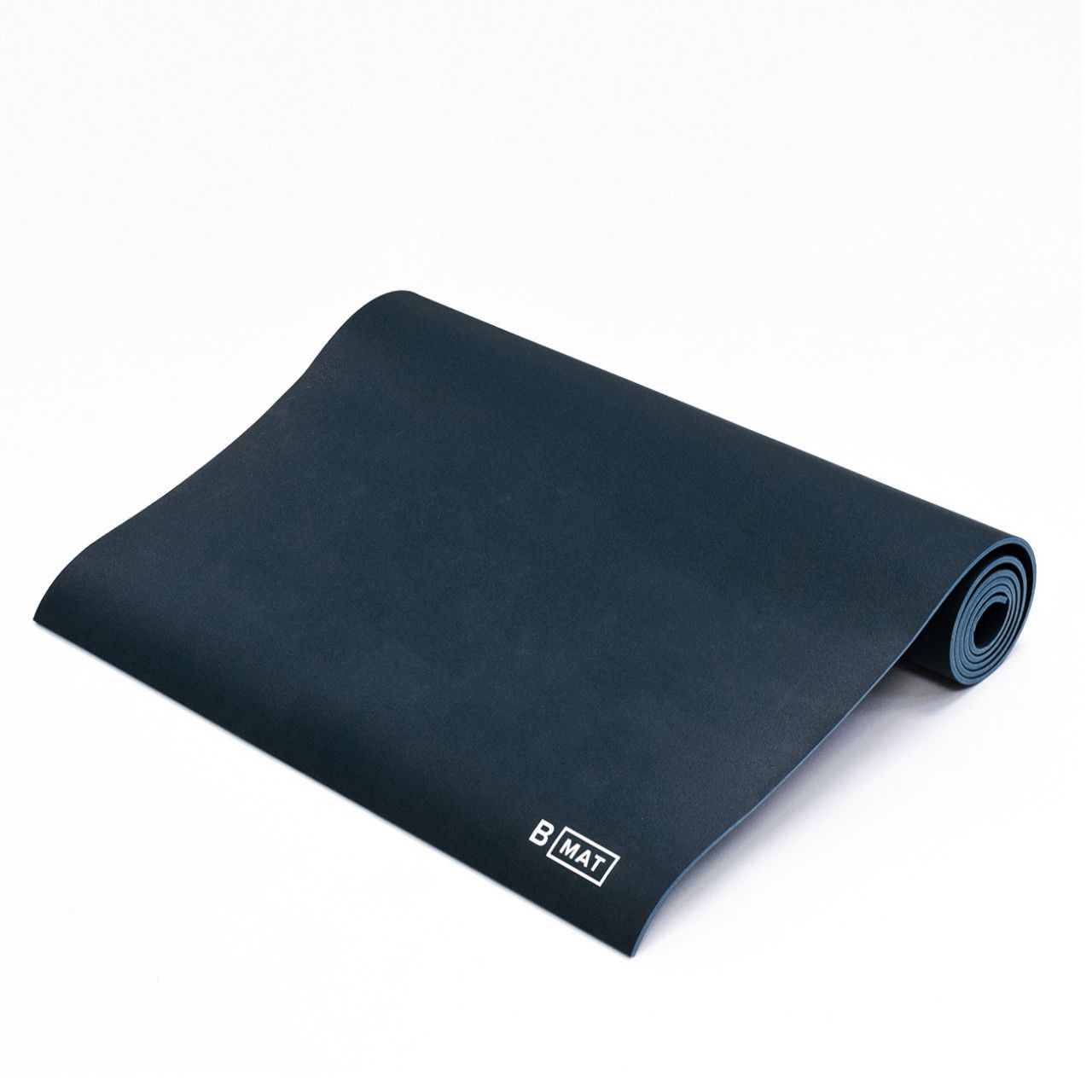 Ausgerollte, graue Yogamatte mit Logo "B MAT" in der Ecke. Auf weißem Hintergrund.