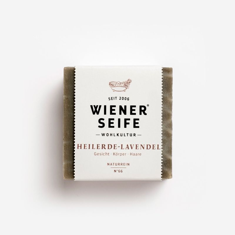 Seife mit Papierbanderole. Aufschrift: Wiener Seife, Heilerde-Lavendel, Naturrein, N°66. Logo mit Badewanne.
