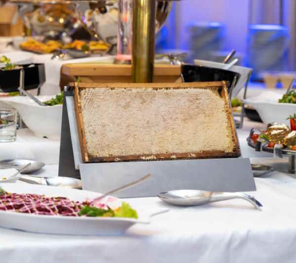 Honigwabe in Holzrahmen auf einem Buffet. Präsentiert auf einem Ständer. Umgebung: Speisen, Besteck.