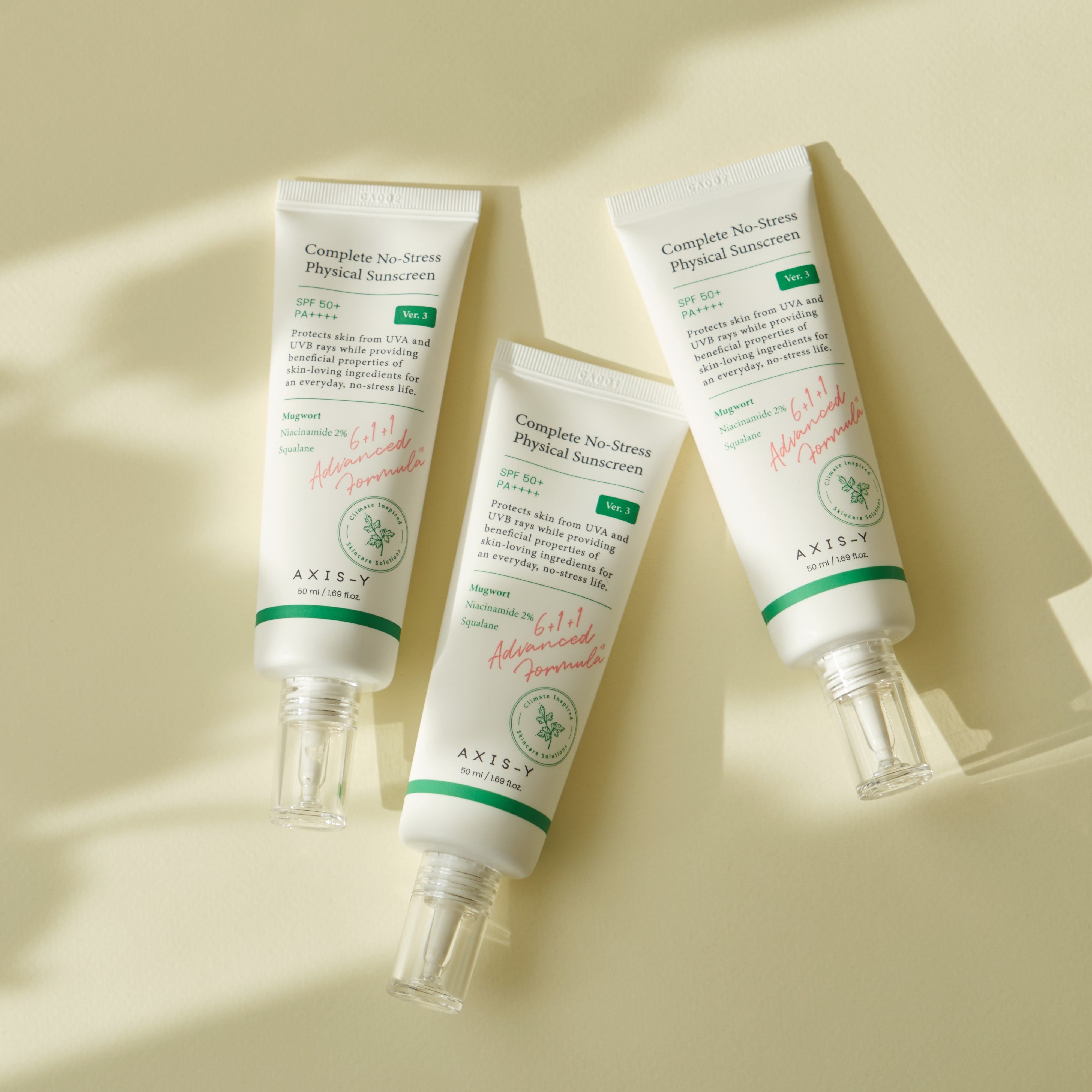 Drei Tuben AXIS-Y Complete No-Stress Physical V.3 SPF 50. Weiß mit grünen Akzenten. Auf hellem Untergrund.