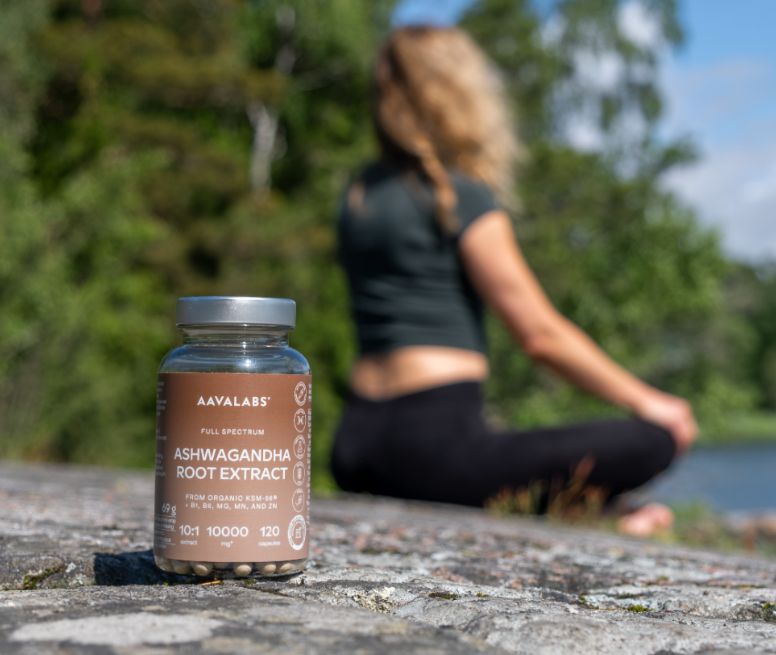 Aavalabs Ashwagandha KSM 66 Flasche auf Felsen, Frau meditiert im Hintergrund.