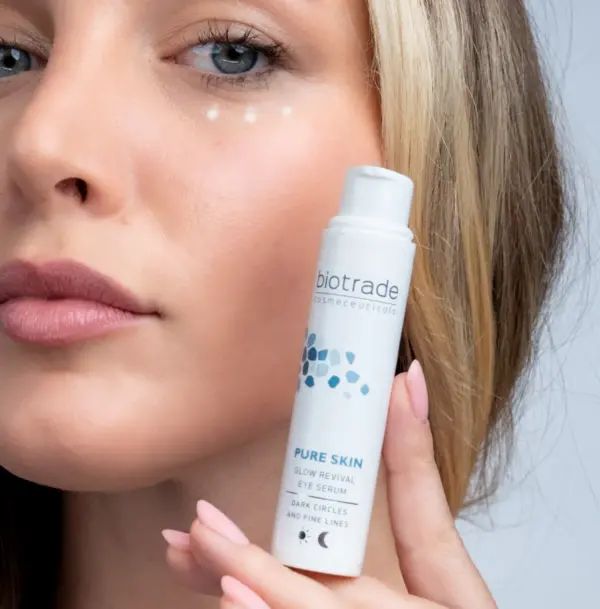 Frau hält weißen Zylinder, Biotrade-Logo, Pure Skin Glow Revival Eye Serum, gegen Schwellungen, Augenringe und feine Linien.