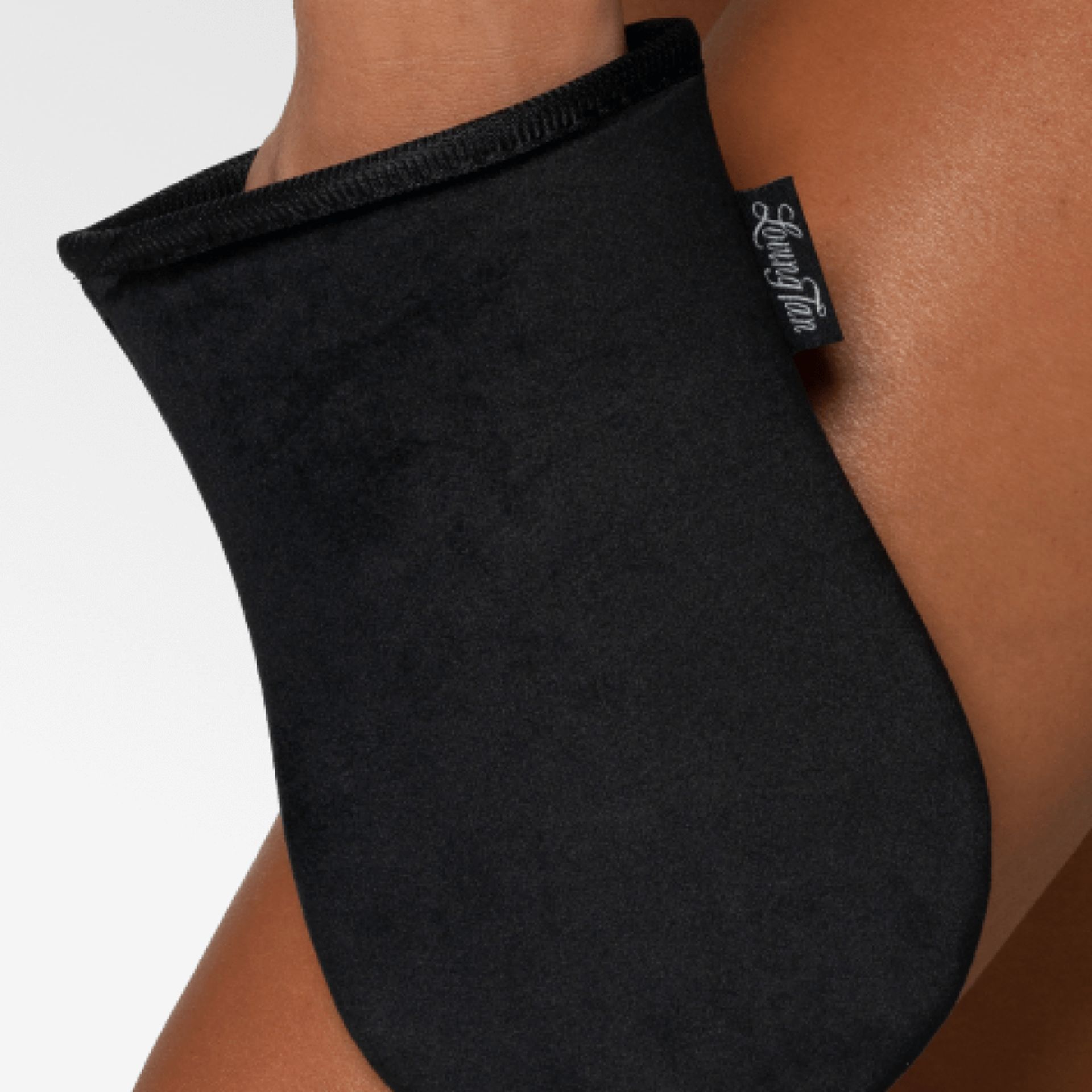 Schwarzer Applikator-Handschuh auf Bein. Schwarzes Material, Label mit Logo. Der Handschuh bedeckt die Hand und einen Teil des Unterarms.