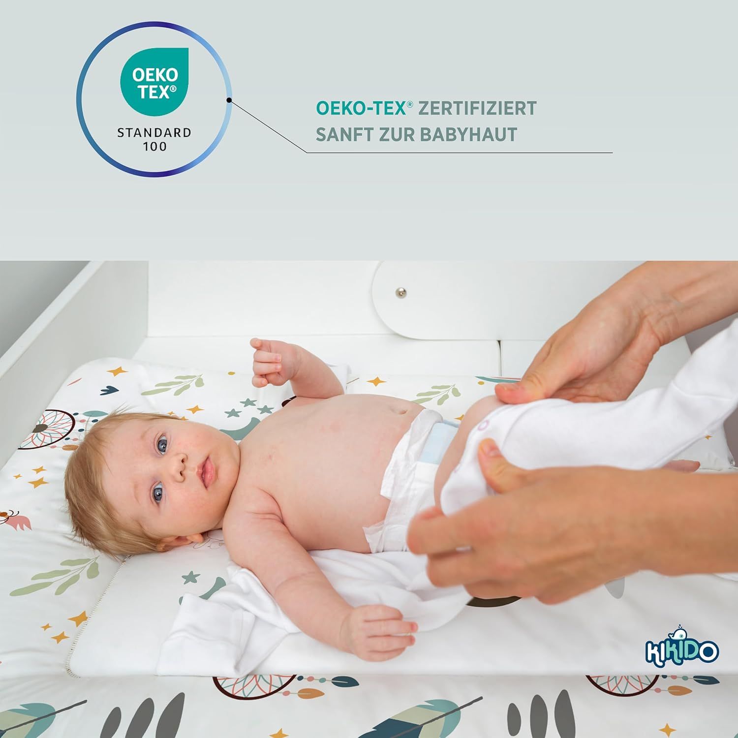 Baby liegt auf Wickelauflage. Text: OEKO-TEX® zertifiziert. Sanft zur Babyhaut. Kikido Logo.